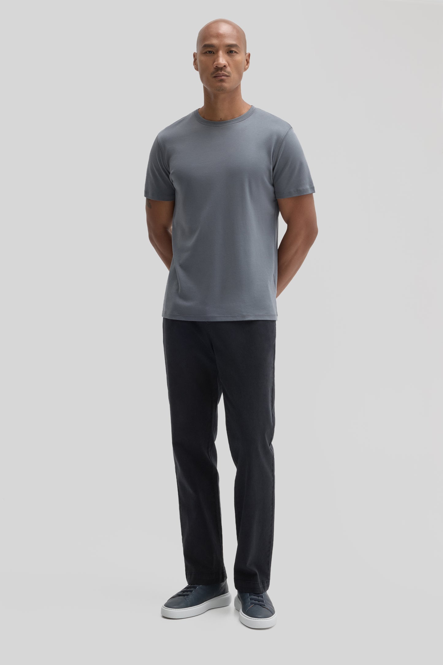 Man wearing gray short-sleeve crew neck t-shirt with black pants and navy sneakers.
