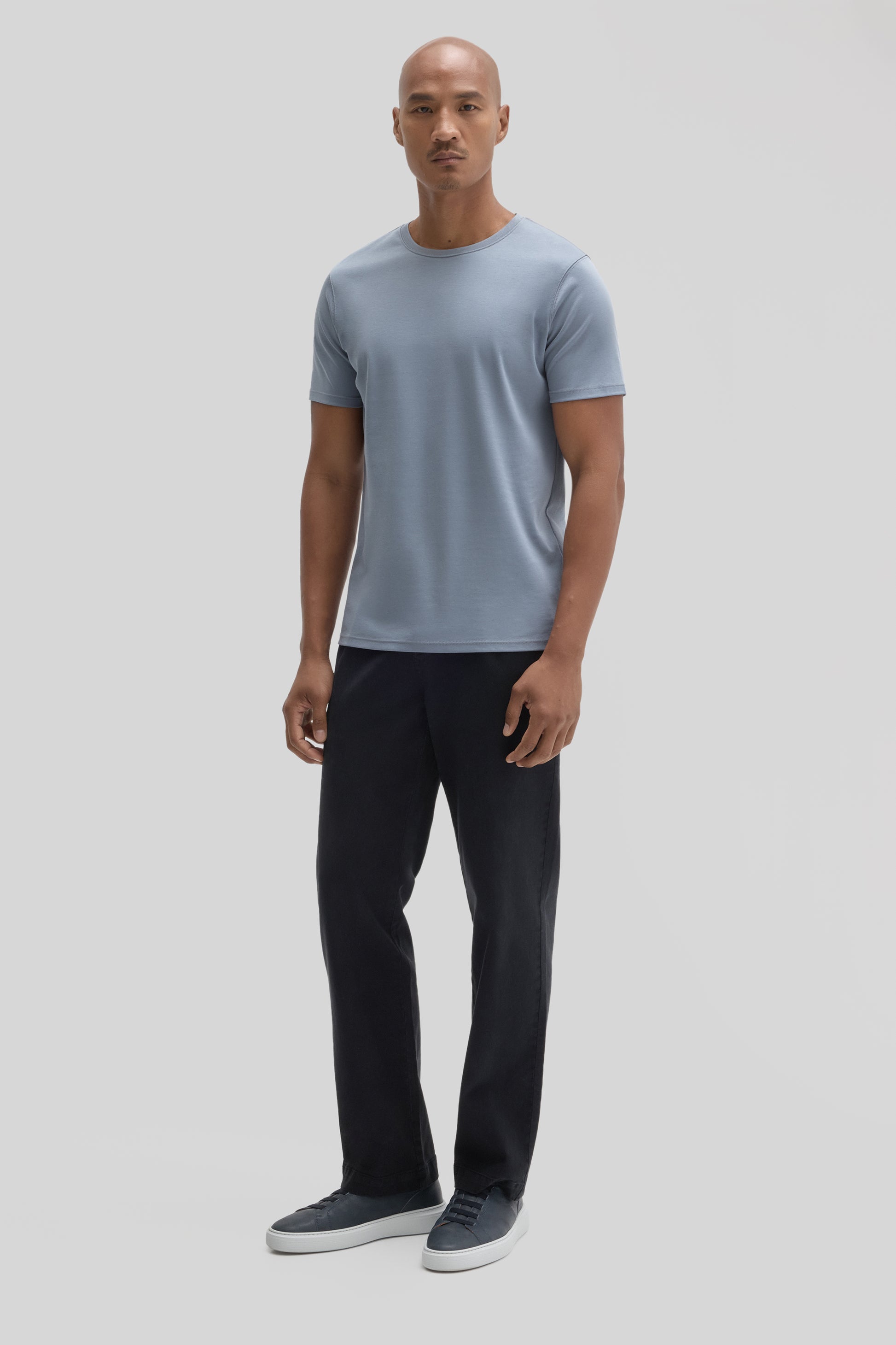 Man wearing light blue crew-neck t-shirt with black pants and gray sneakers.