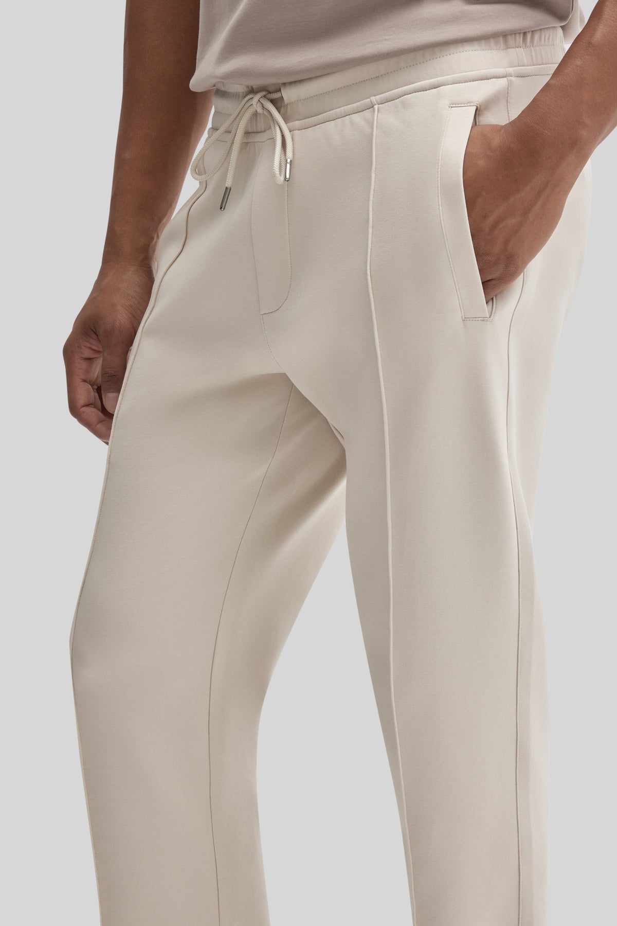 Cream jogging pants with drawstring waist, side pockets, and contrast stitching detail on legs.