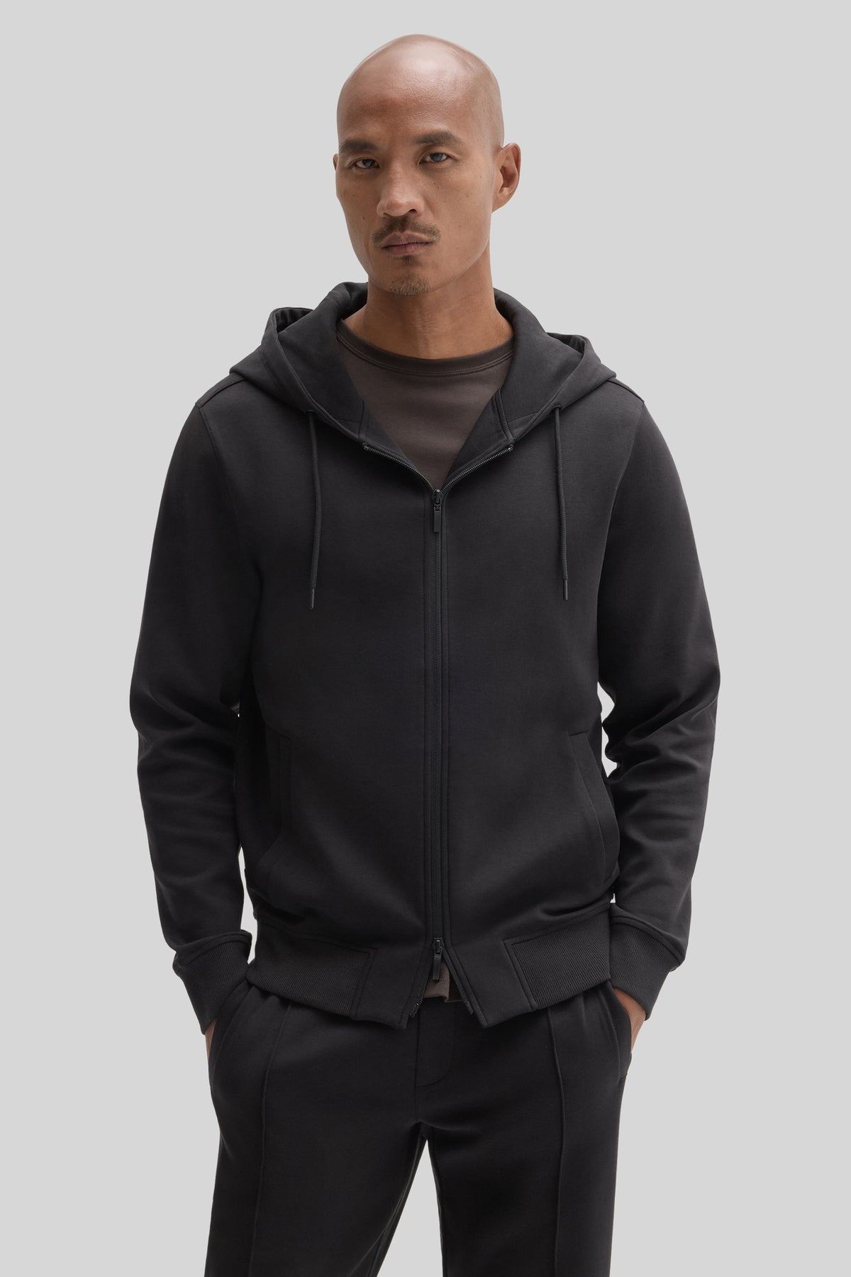 Black full zip hoodie with drawstring hood and front pockets, worn with matching black pants.