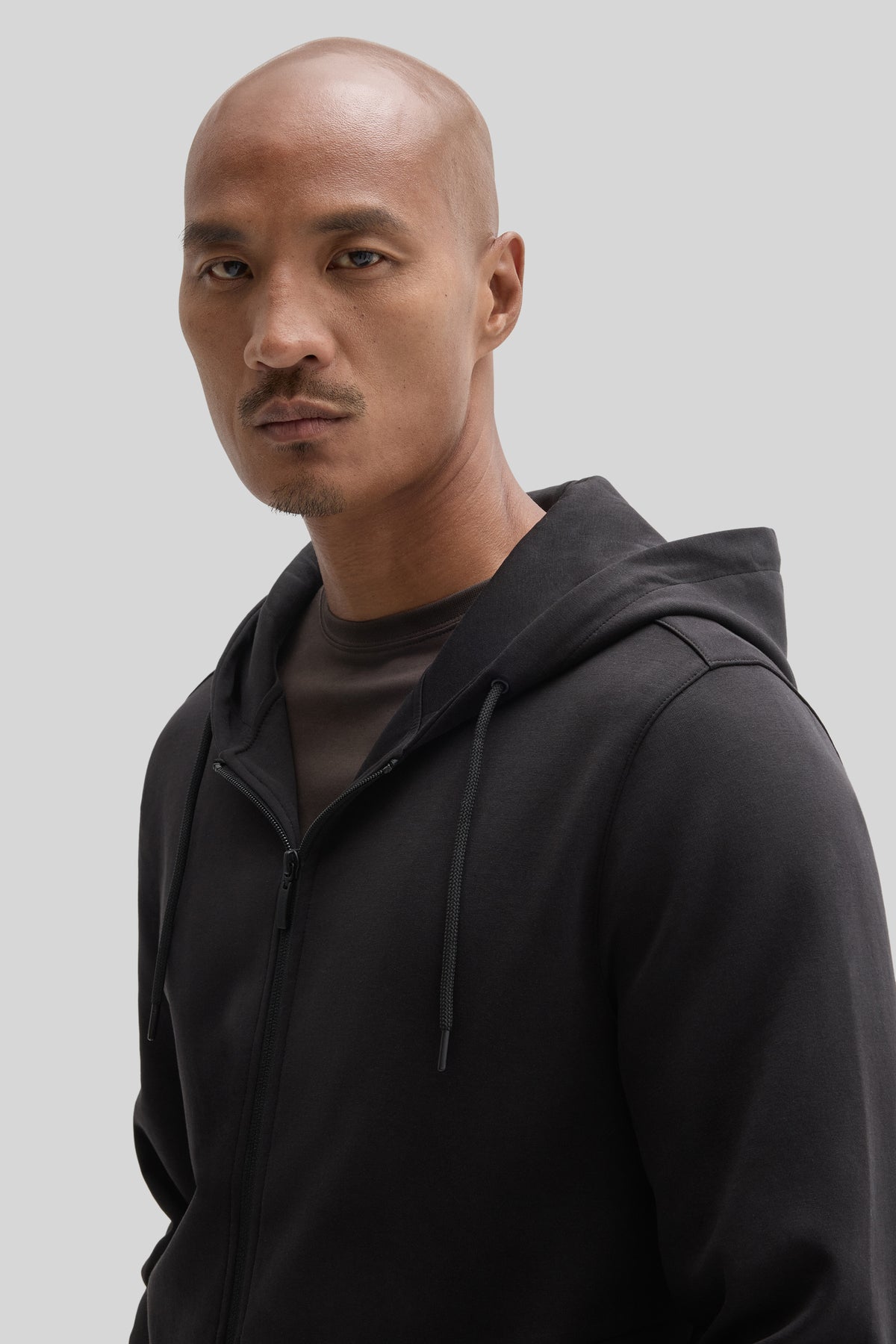 Man wearing black full zip hoodie with drawstrings over dark shirt.