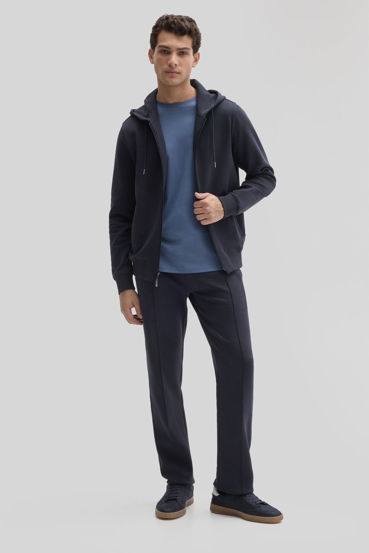 Man wearing black full zip hoodie with drawstring hood over blue t-shirt and dark pants.