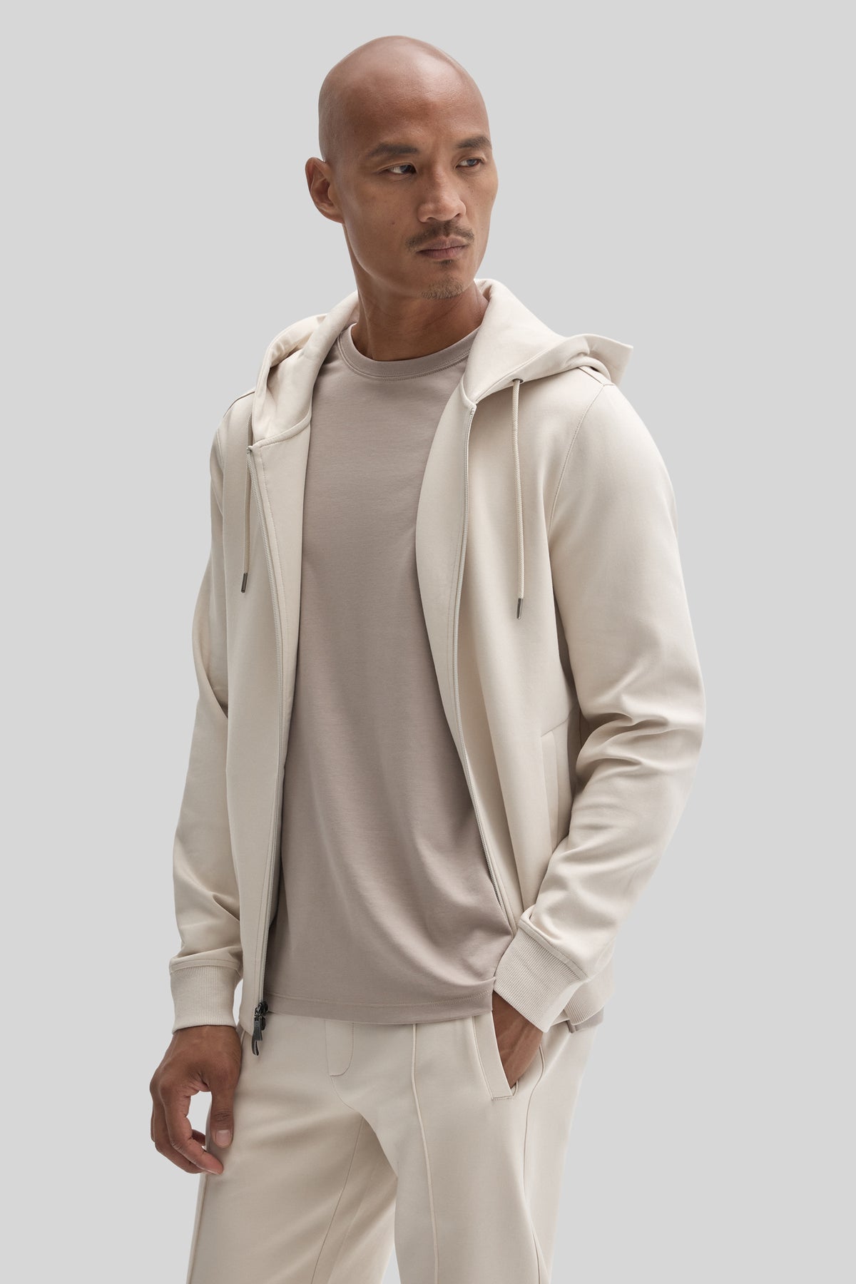 Man wearing cream full zip hoodie over gray t-shirt with matching cream pants.