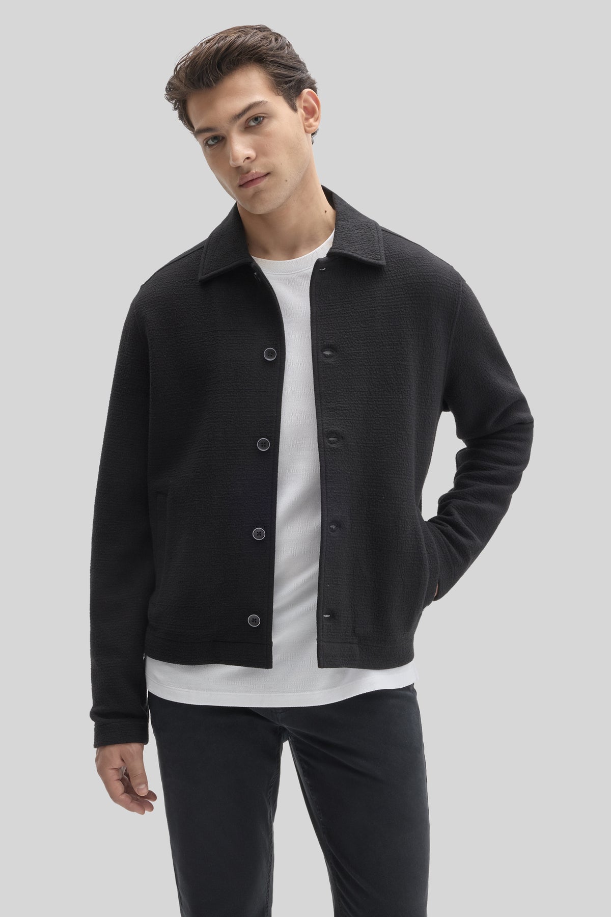 Black buttoned jacket with textured fabric worn over white t-shirt and dark pants.