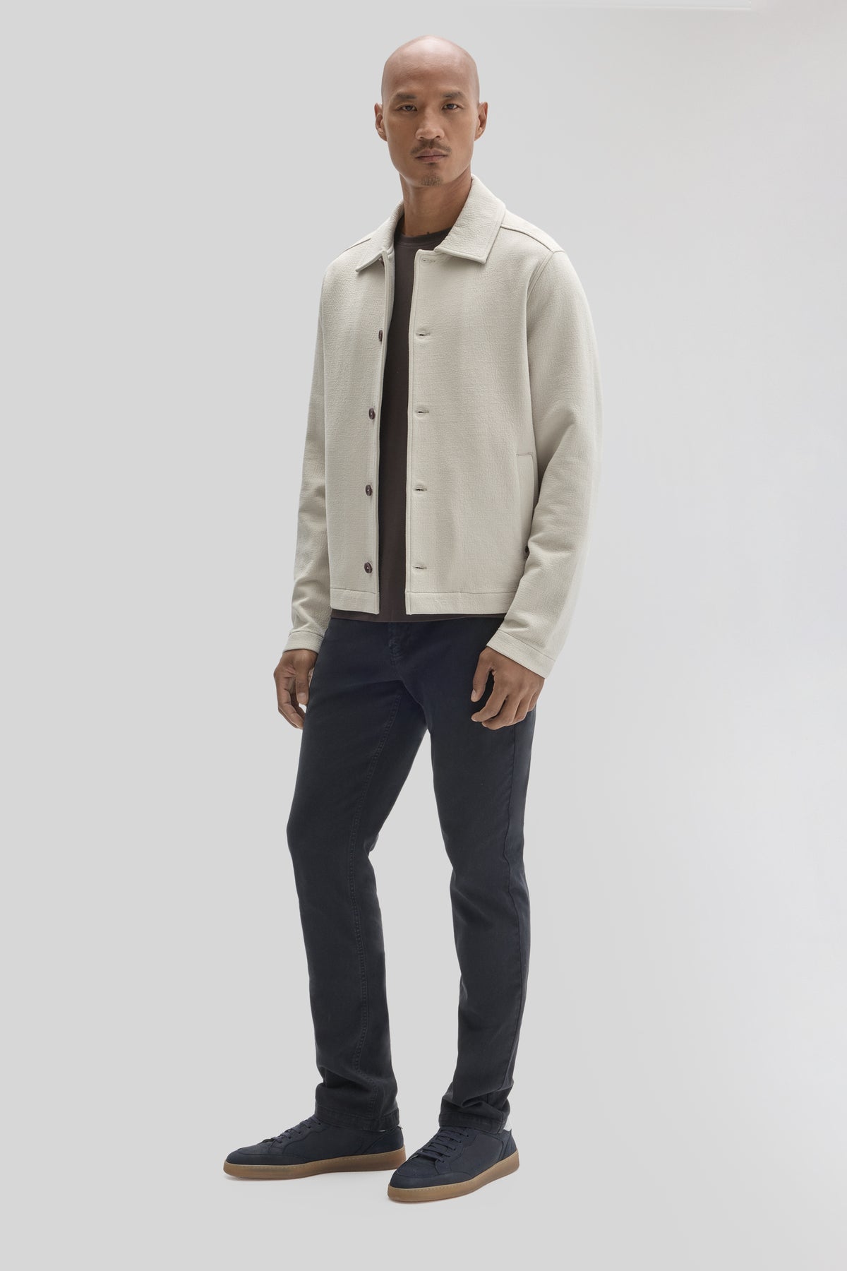 Cream-colored buttoned jacket with collar worn over black shirt and dark jeans.