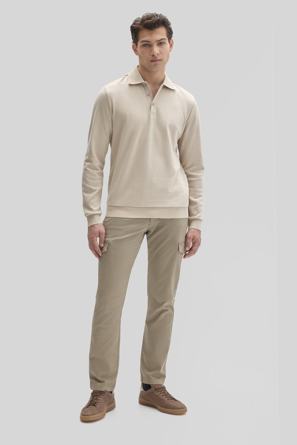 Man wearing cream long sleeve polo shirt with collar and buttons, paired with beige cargo pants and brown shoes.