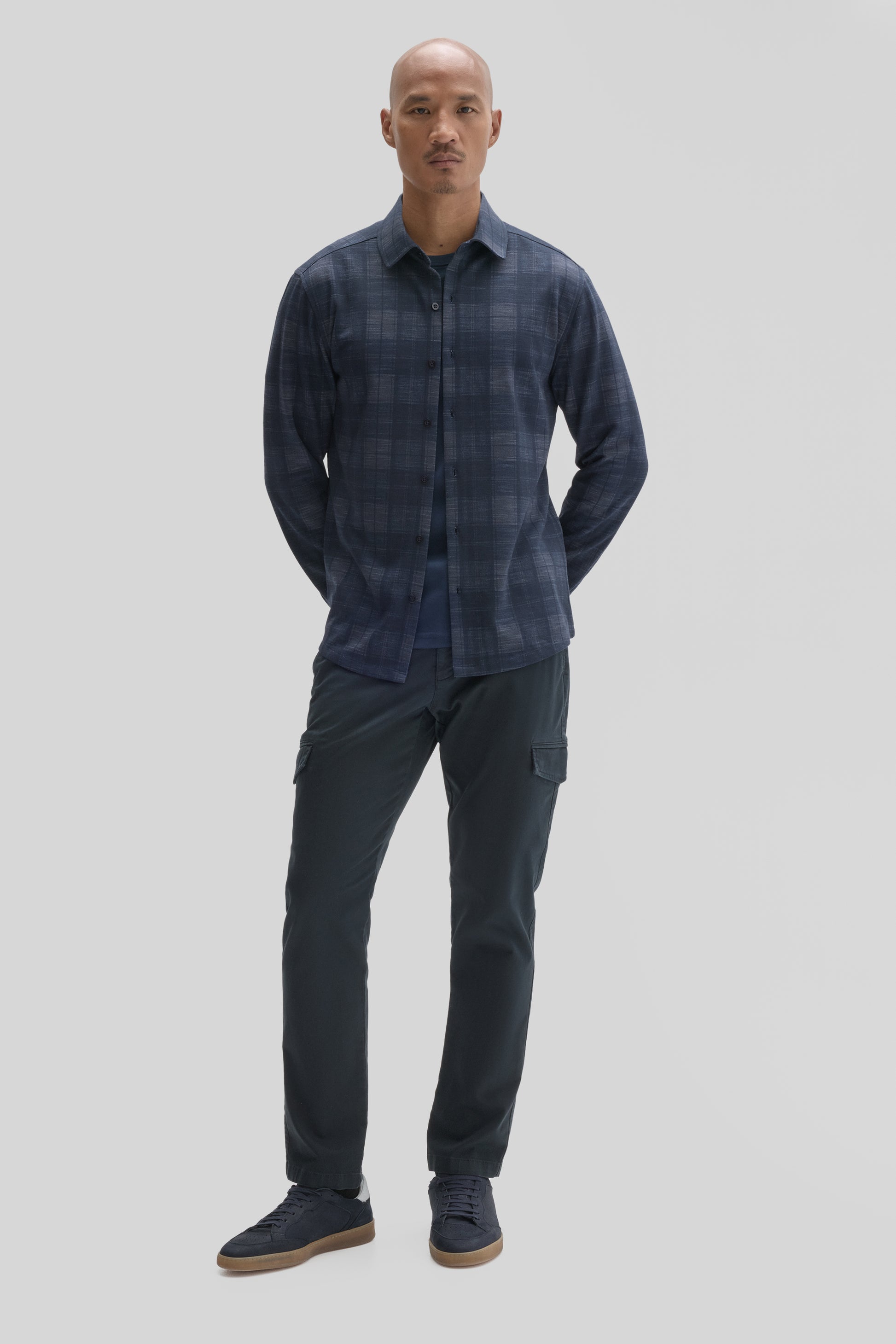 Man wearing navy plaid button-up shirt with long sleeves over a darker undershirt and black cargo pants.