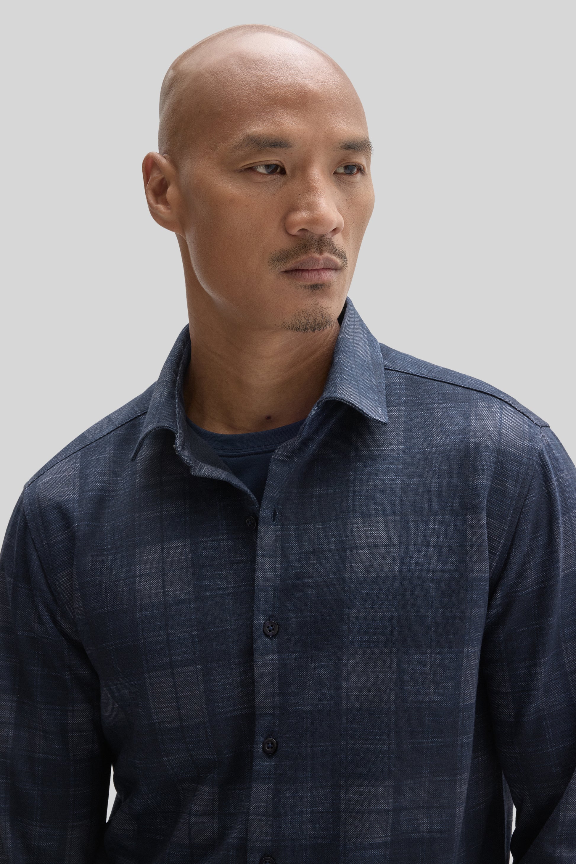 Man wearing navy blue knit shirt with subtle plaid pattern and button front closure.