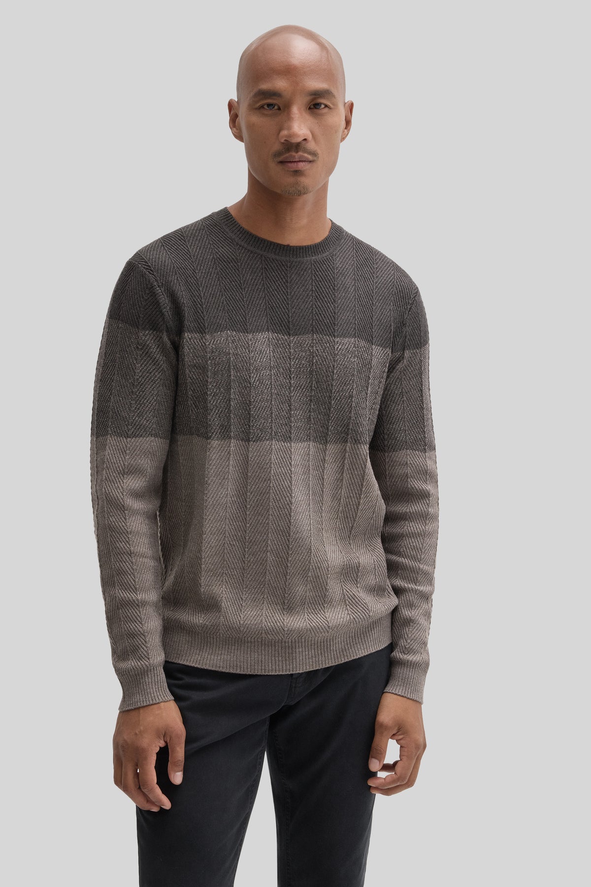 Gray herringbone crewneck sweater with horizontal color-block stripes worn with black pants.