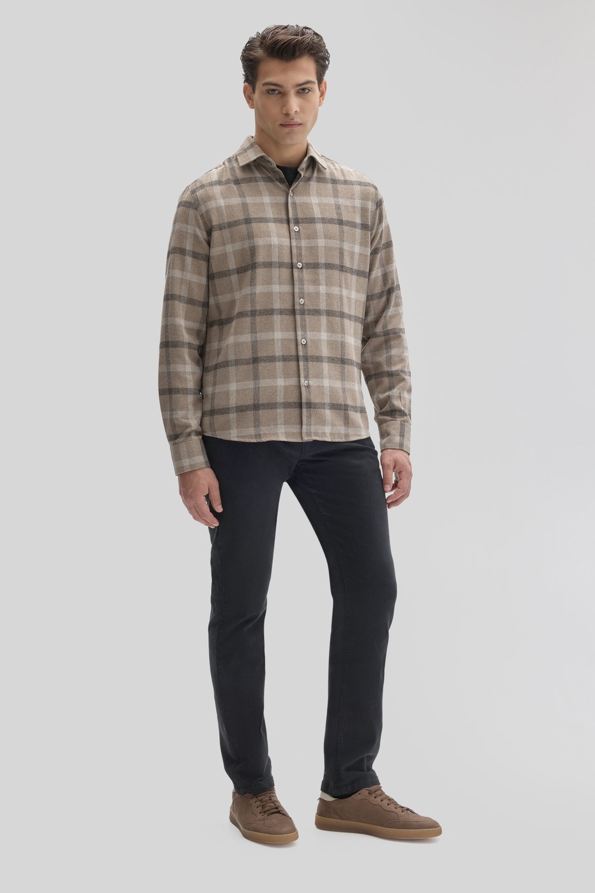 Man wearing tan and gray plaid flannel shirt with white buttons and black pants.