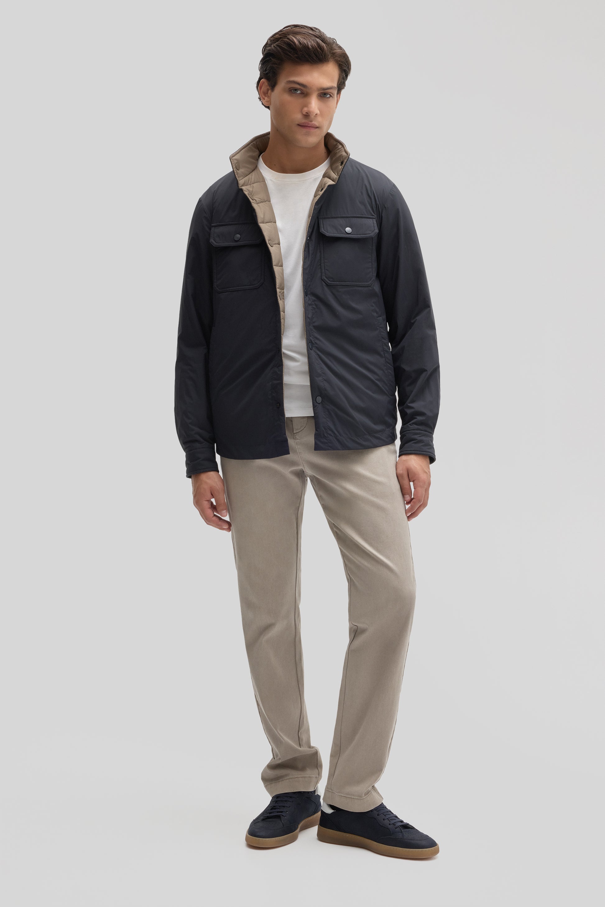 Man wearing black and tan reversible snap jacket with chest pockets over white shirt and beige pants.