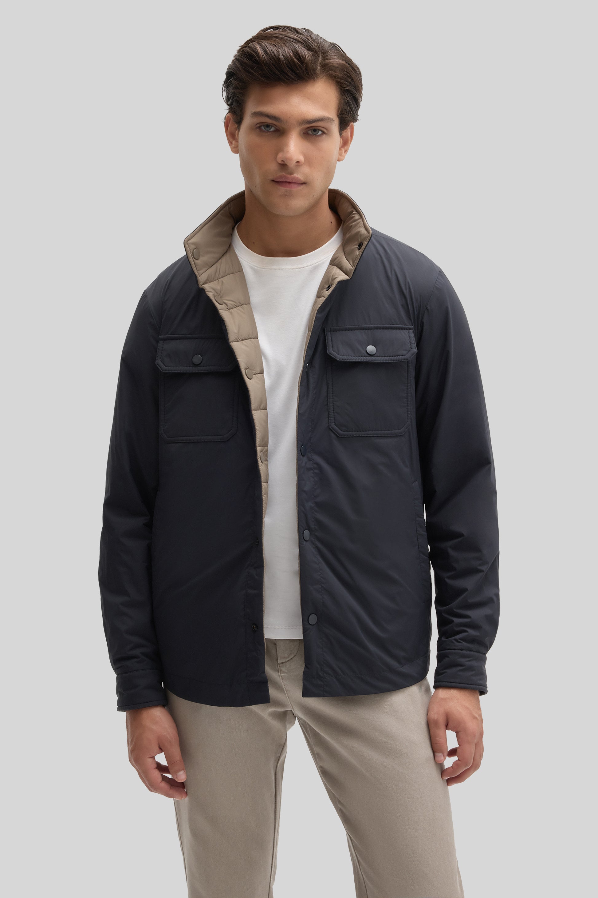 Man wearing black reversible snap jacket with beige interior, paired with white shirt and khaki pants.