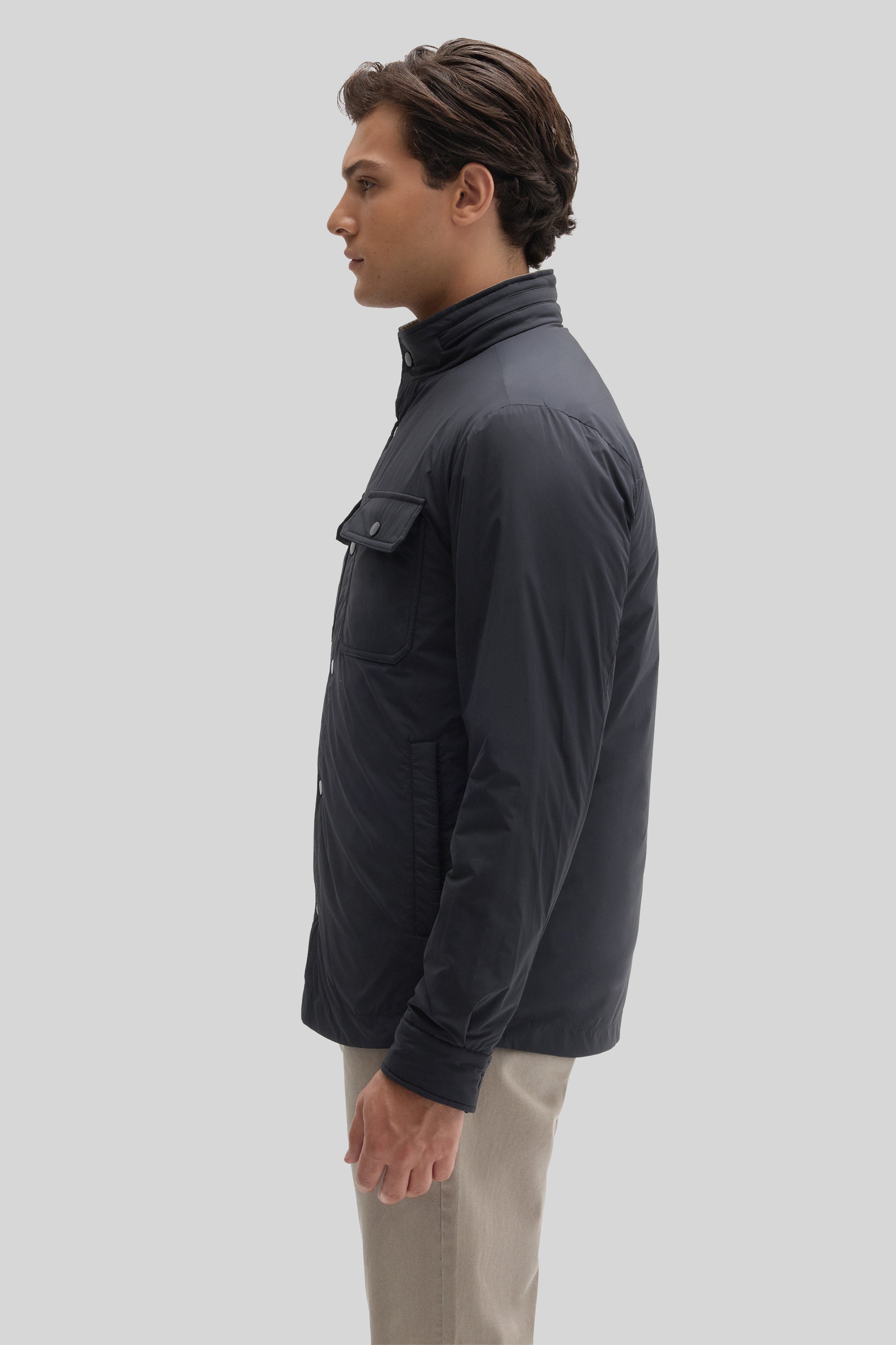 Black nylon snap jacket with high collar and chest pocket, worn by man in side profile view.