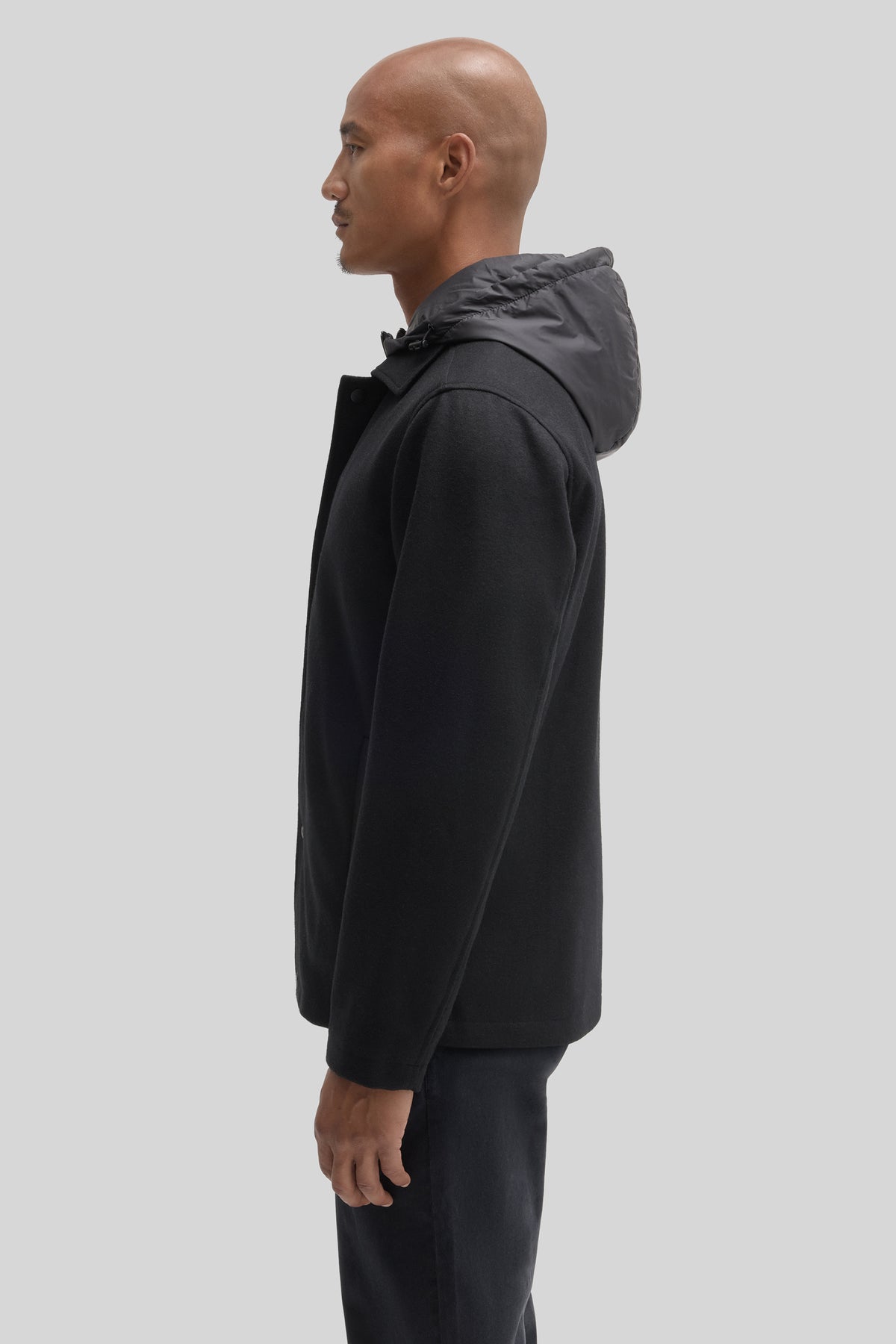 Man wearing black car coat with quilted hood, shown in profile view.