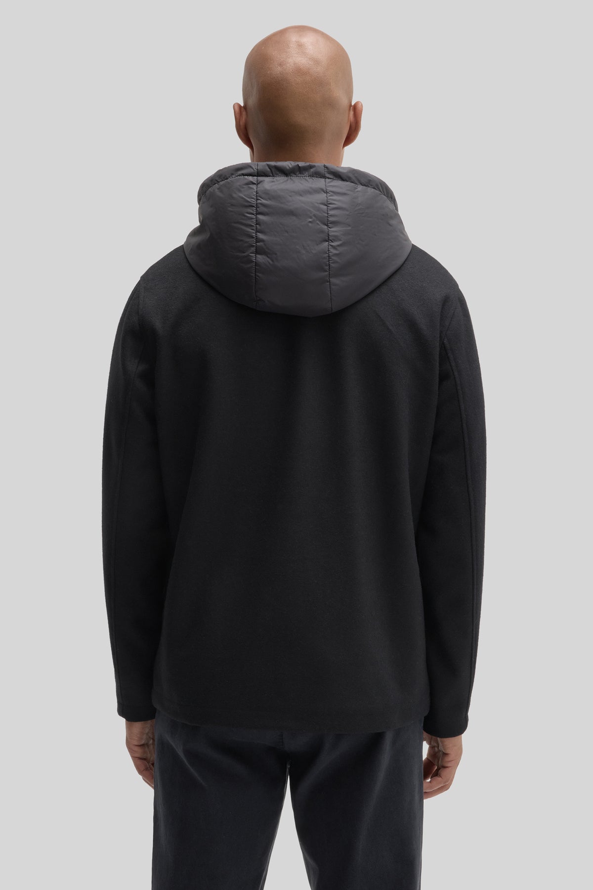 Black car coat with quilted hood and knit body, shown from back on model.