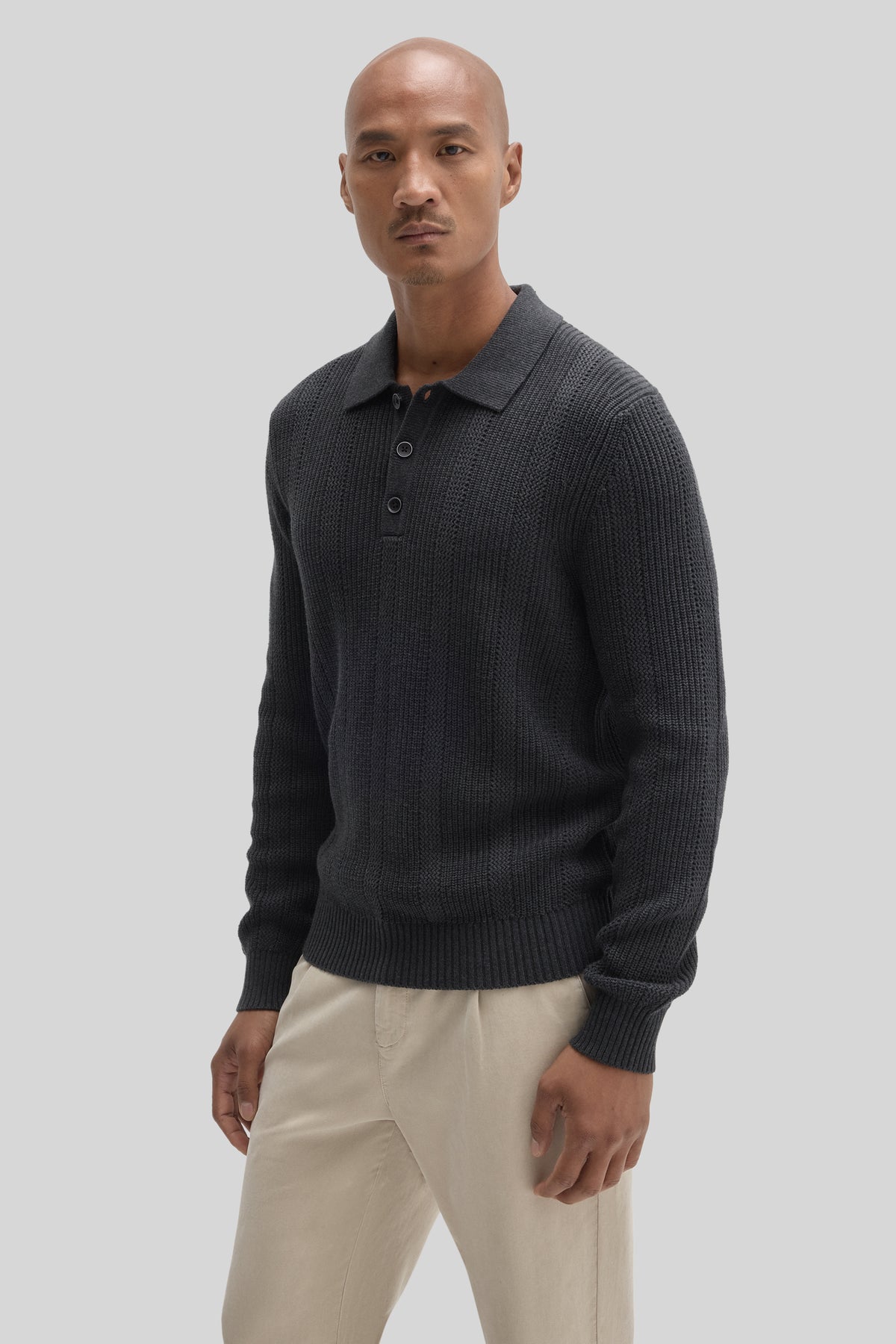 Man wearing dark gray ribbed sweater polo with collar and button front, paired with cream-colored pants.