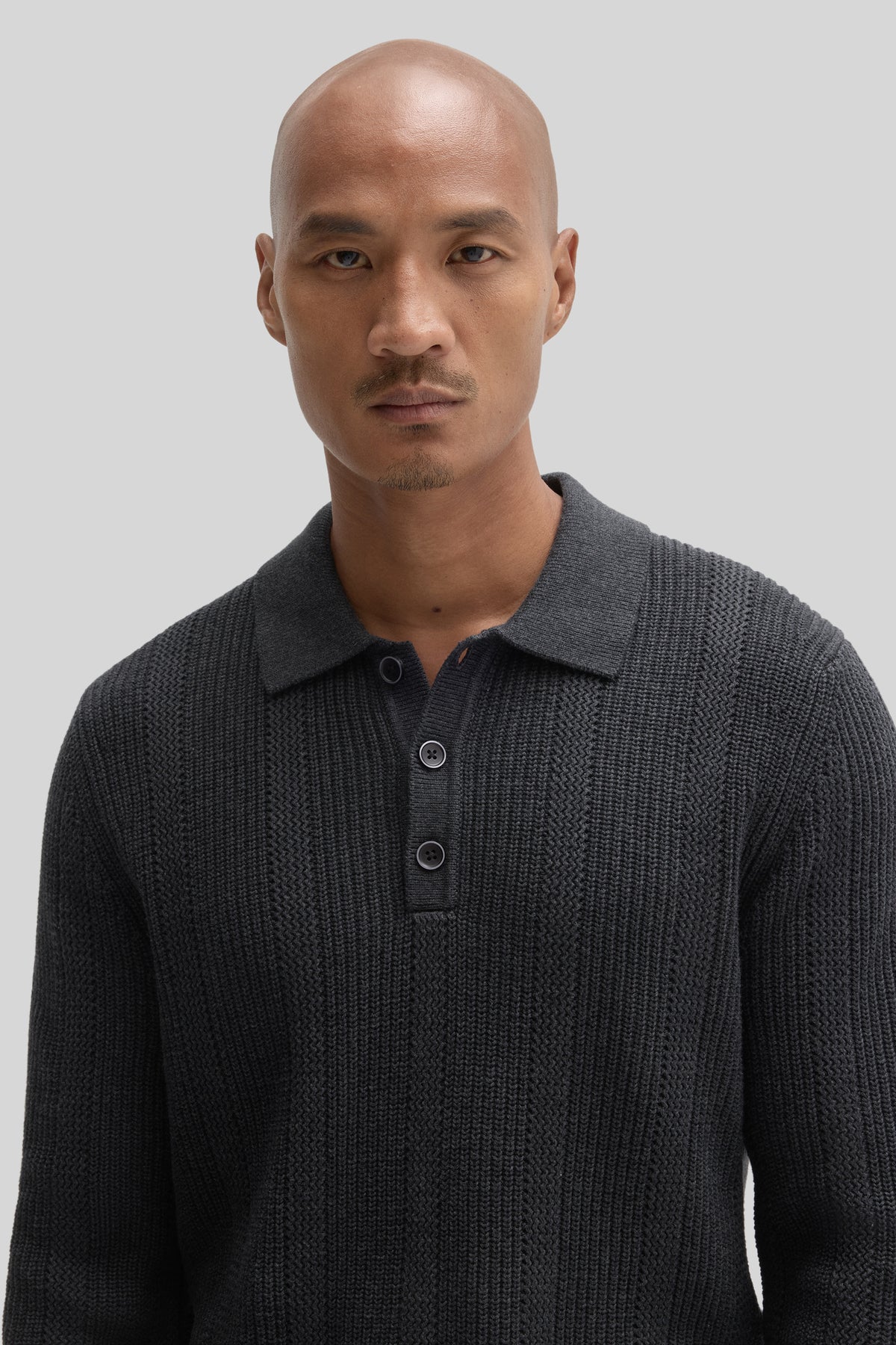 Charcoal gray sweater polo with ribbed texture and button placket at neckline, worn by model against neutral background.