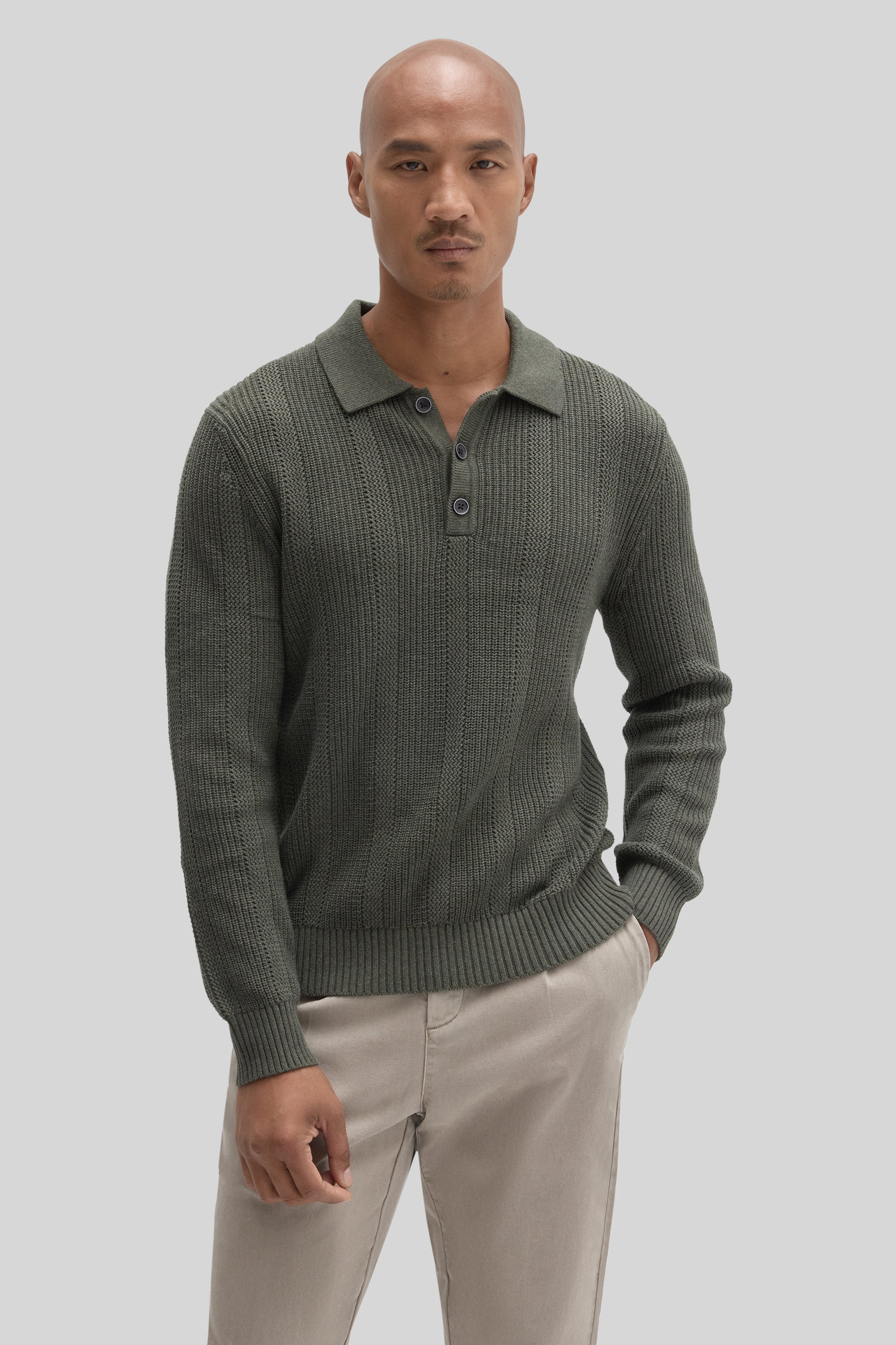 Olive green ribbed sweater polo with collar and button front, paired with cream trousers.