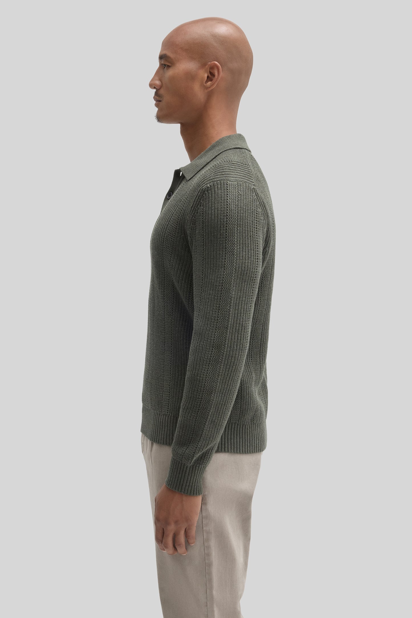 Sage green knit sweater polo with ribbed texture worn with light beige trousers.