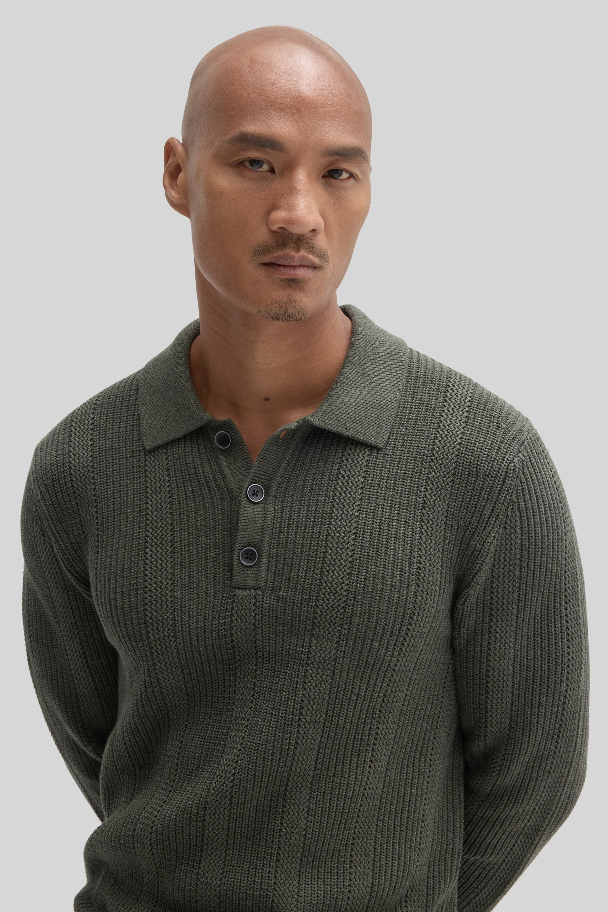 Man wearing sage green textured sweater polo with collar and button placket.