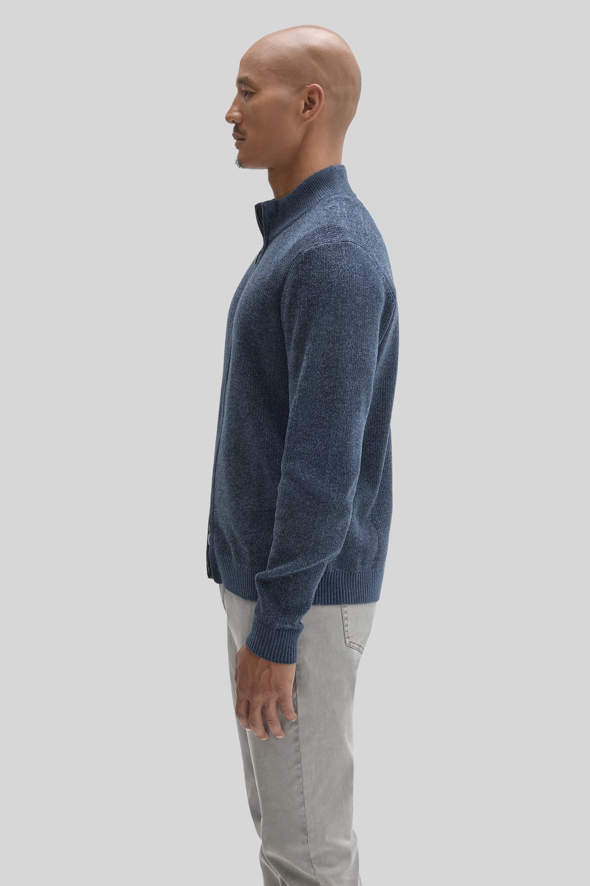 Man wearing blue full-zip mock neck sweater with gray pants, shown in profile view.