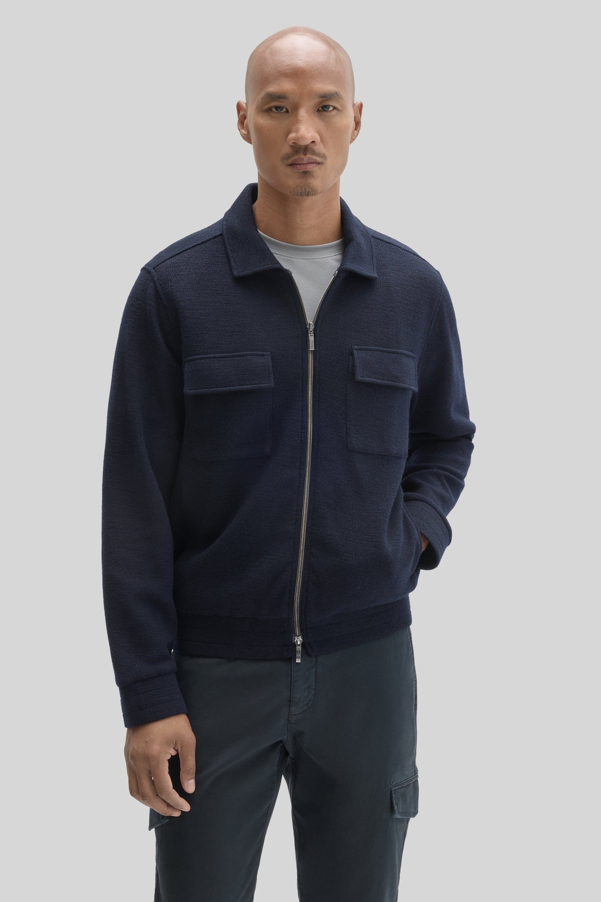 Navy full zip jacket with collared neckline and chest patch pockets worn over gray t-shirt.