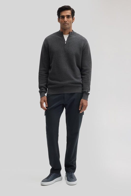 Man wearing dark gray quarter zip sweater with white shirt underneath, paired with black cargo pants and navy sneakers.
