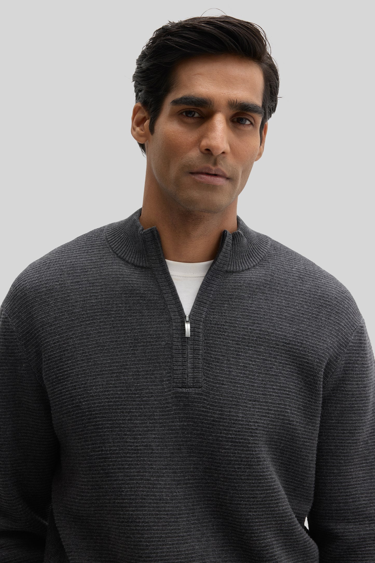 Man wearing dark gray quarter-zip sweater with ribbed texture and white undershirt.
