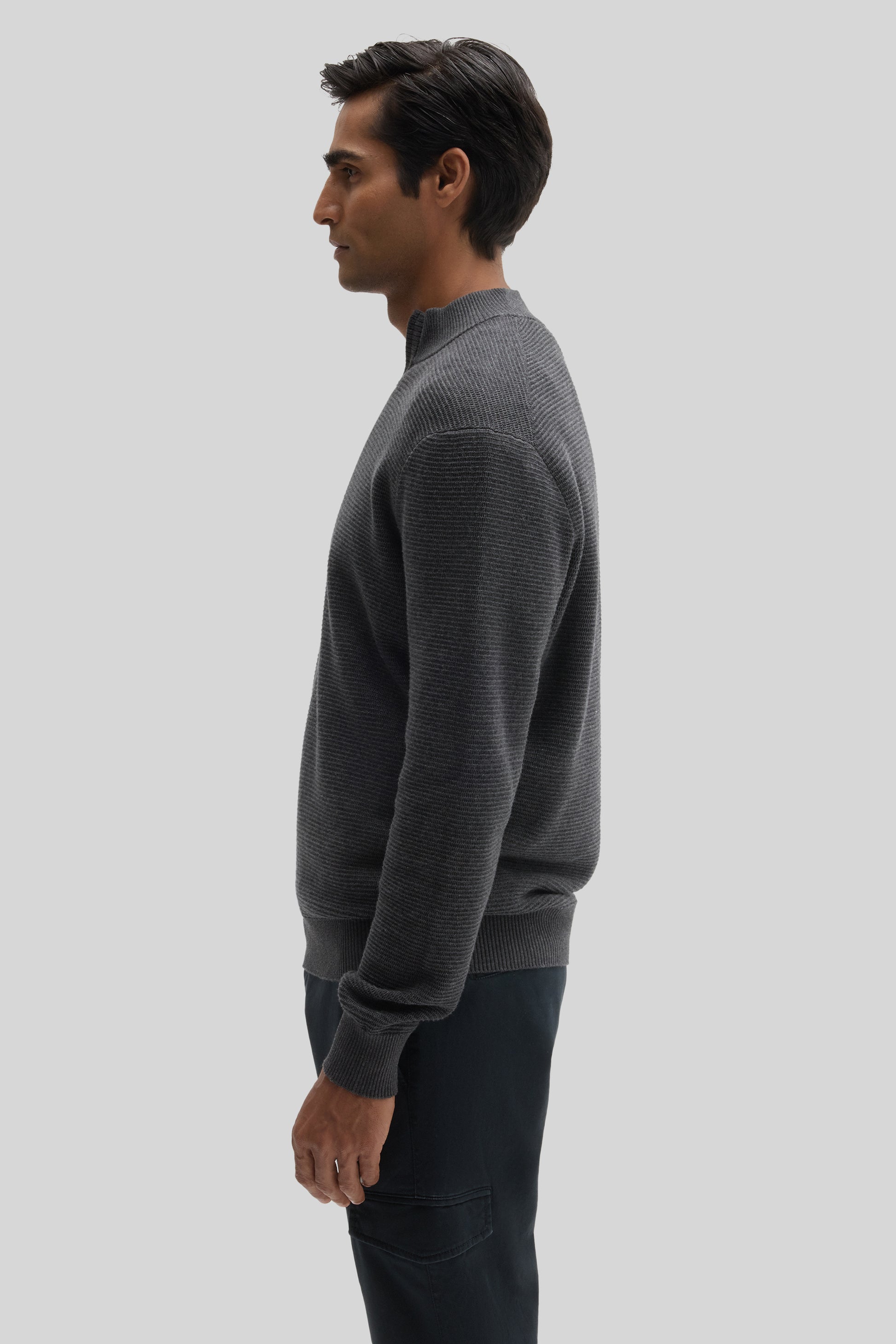 Man wearing gray quarter zip sweater with ribbed texture and black pants, shown in profile view.