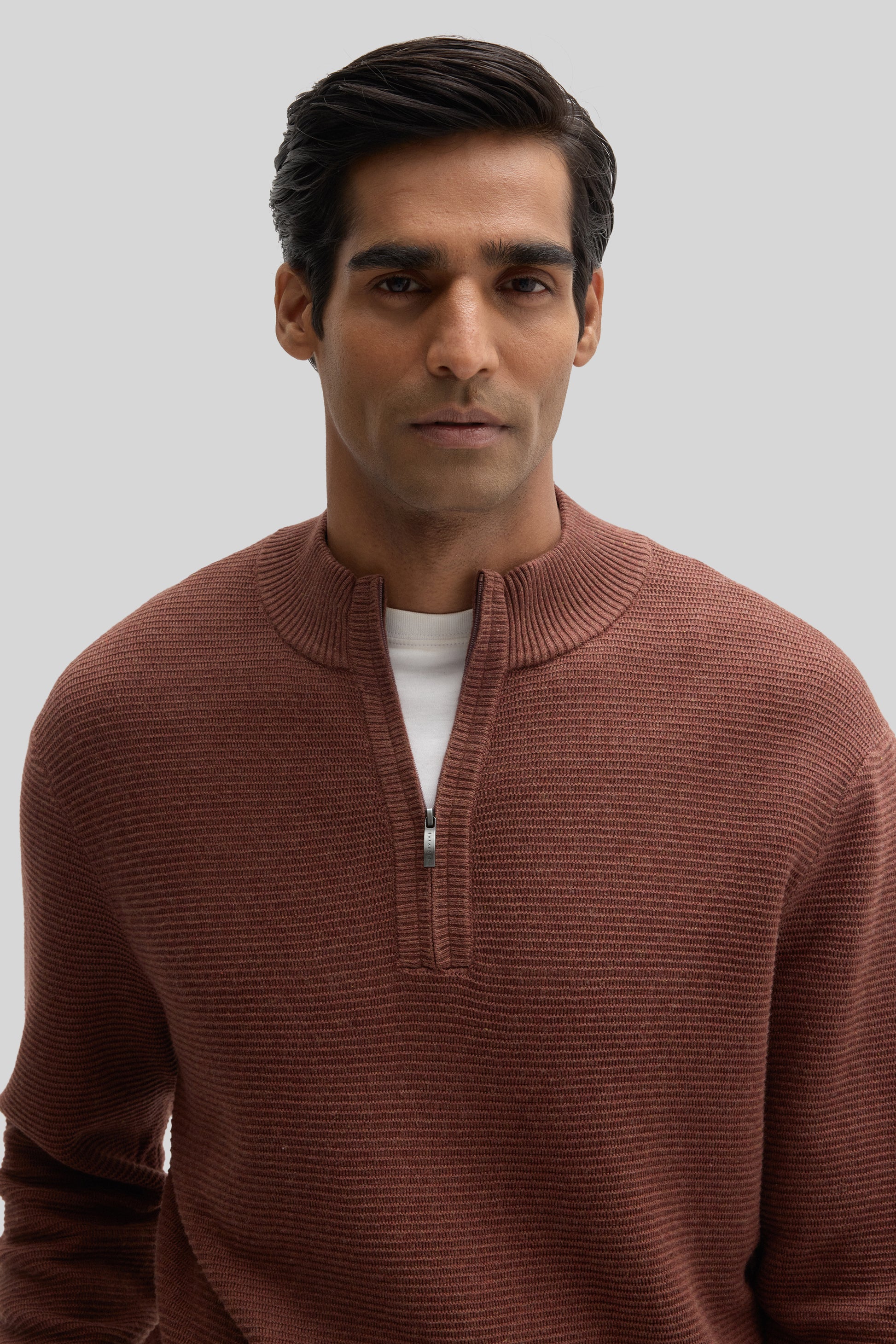 Man wearing a rust-colored quarter-zip sweater with ribbed texture and white undershirt visible at neckline.
