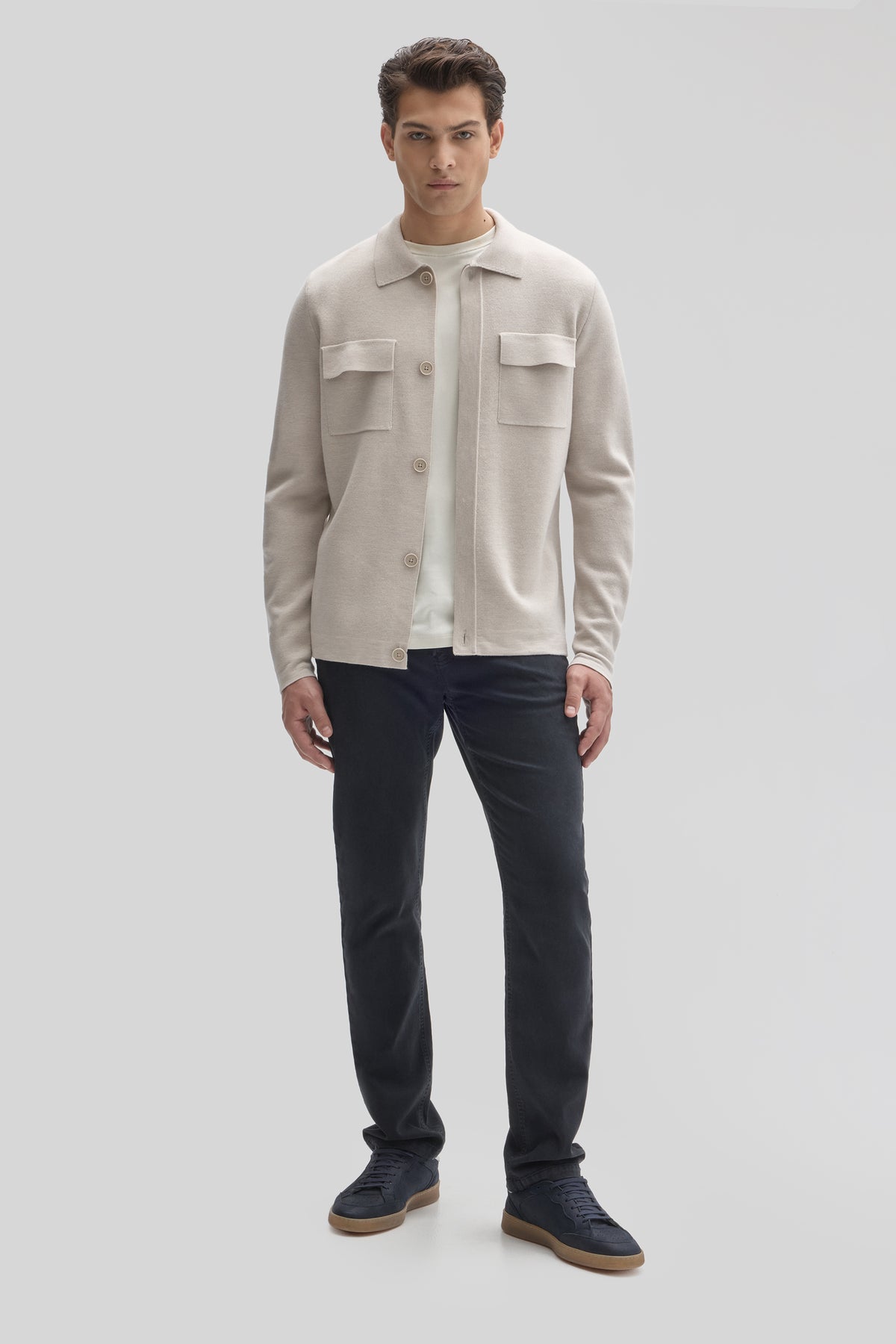 Beige buttoned cardigan with chest pockets worn over white undershirt and dark navy pants.