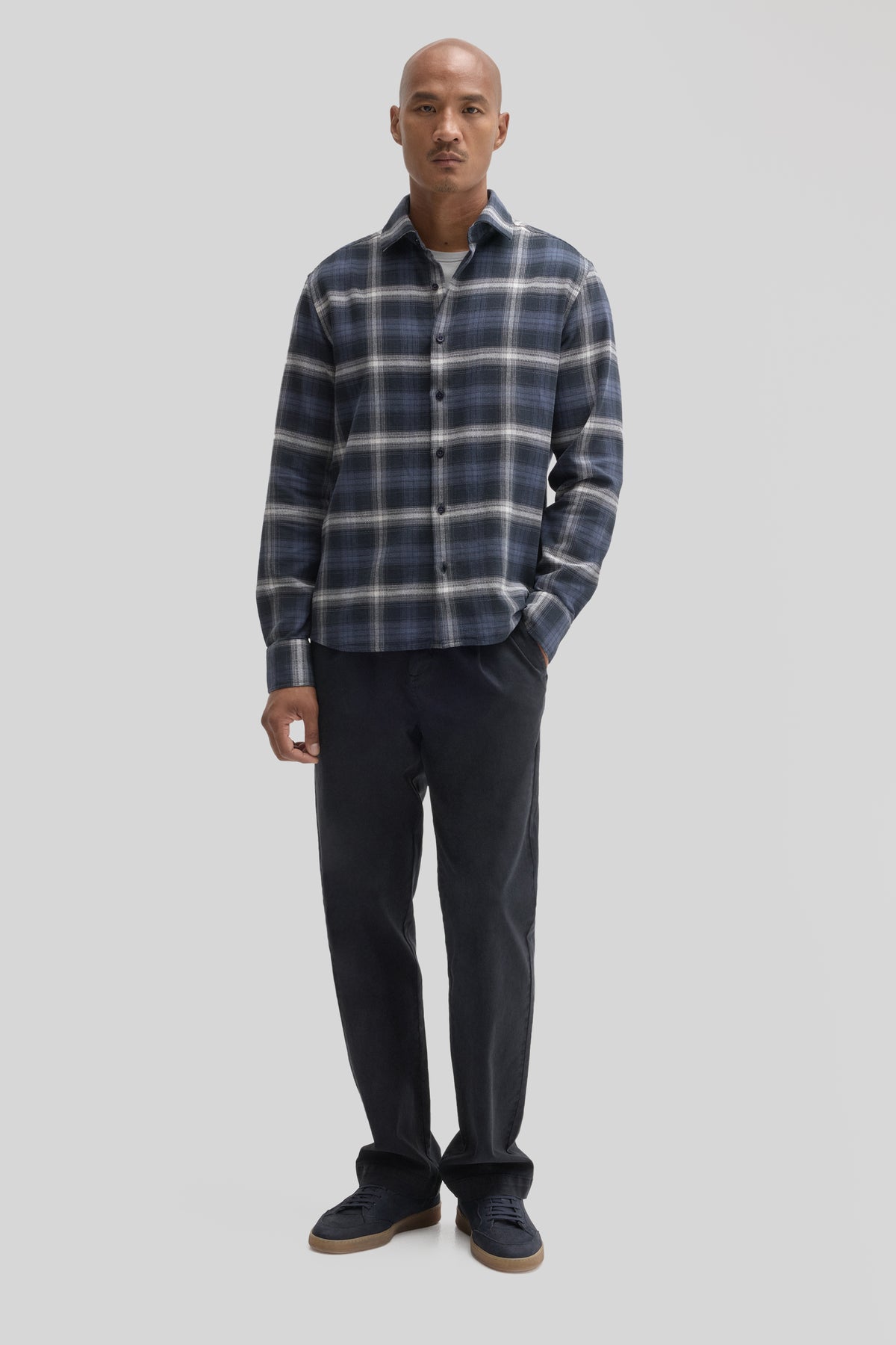 Man wearing navy and white plaid corduroy shirt with button front and long sleeves, paired with black trousers.