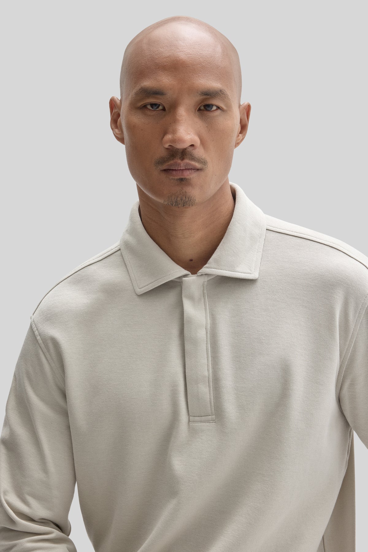 Cream-colored long-sleeve polo shirt with snap button closure and ribbed texture worn by man against neutral background.