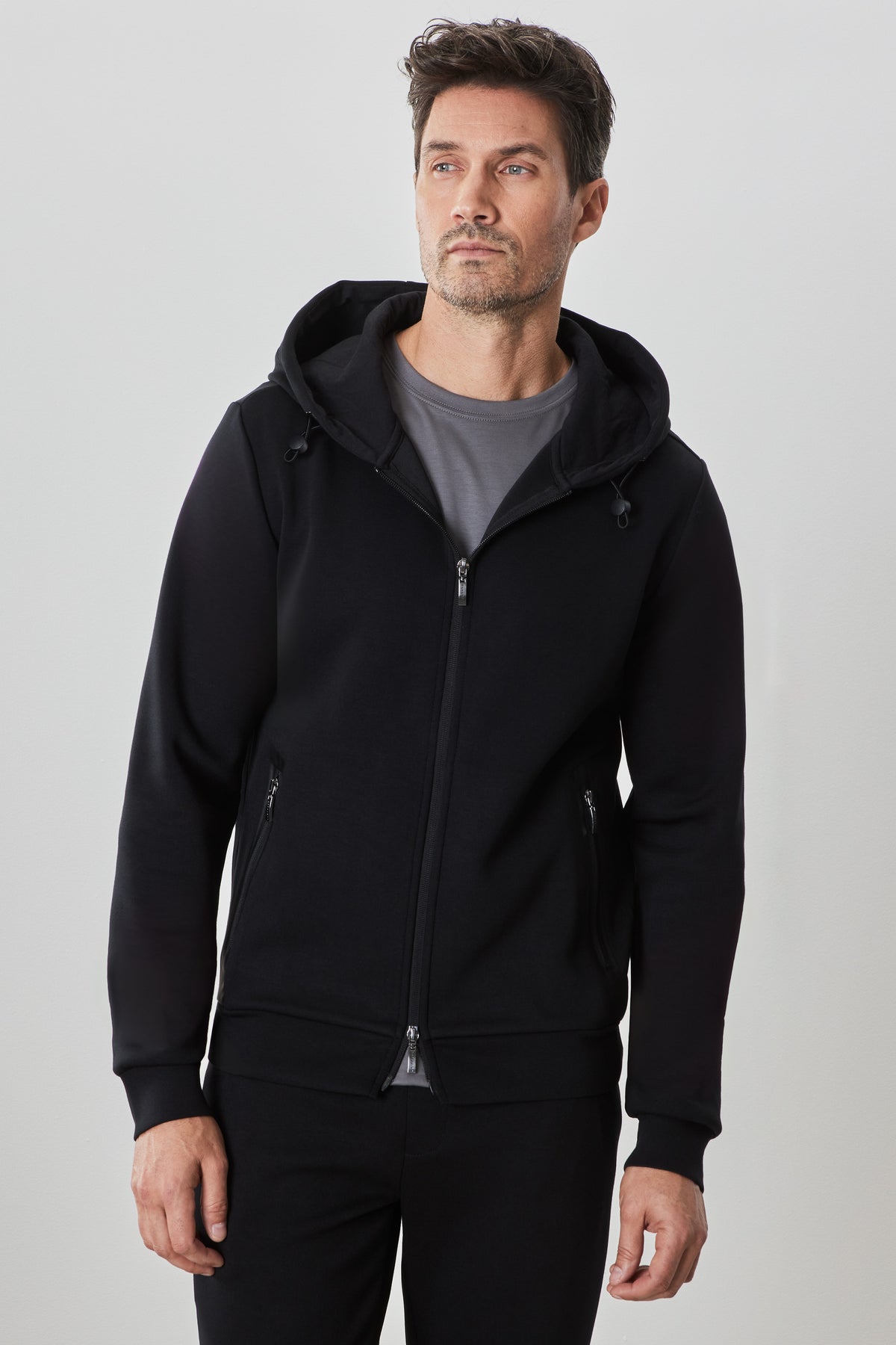 Black zip hoodie with drawstring hood and side pockets worn over gray t-shirt.