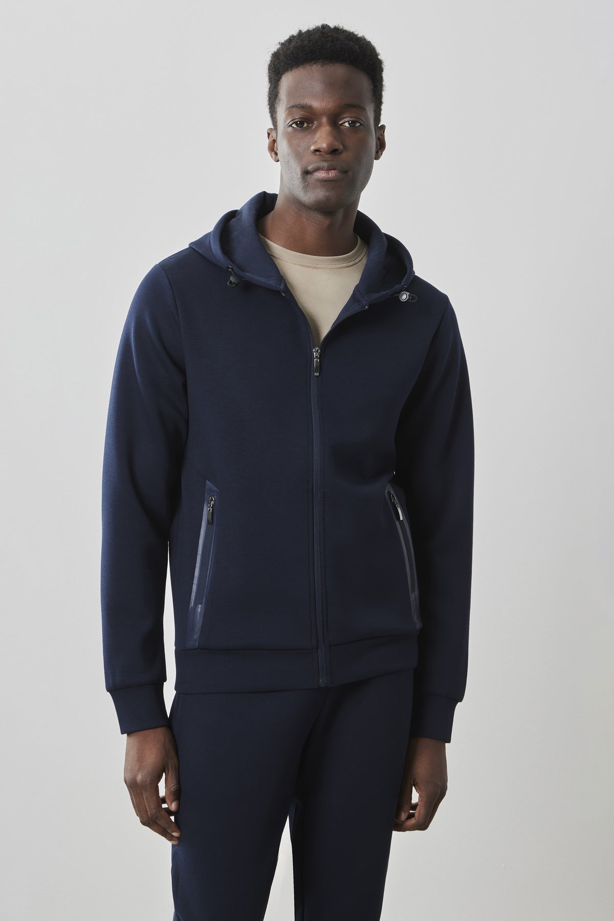 Navy zip hoodie with hood, front pockets, and ribbed cuffs worn over cream t-shirt.