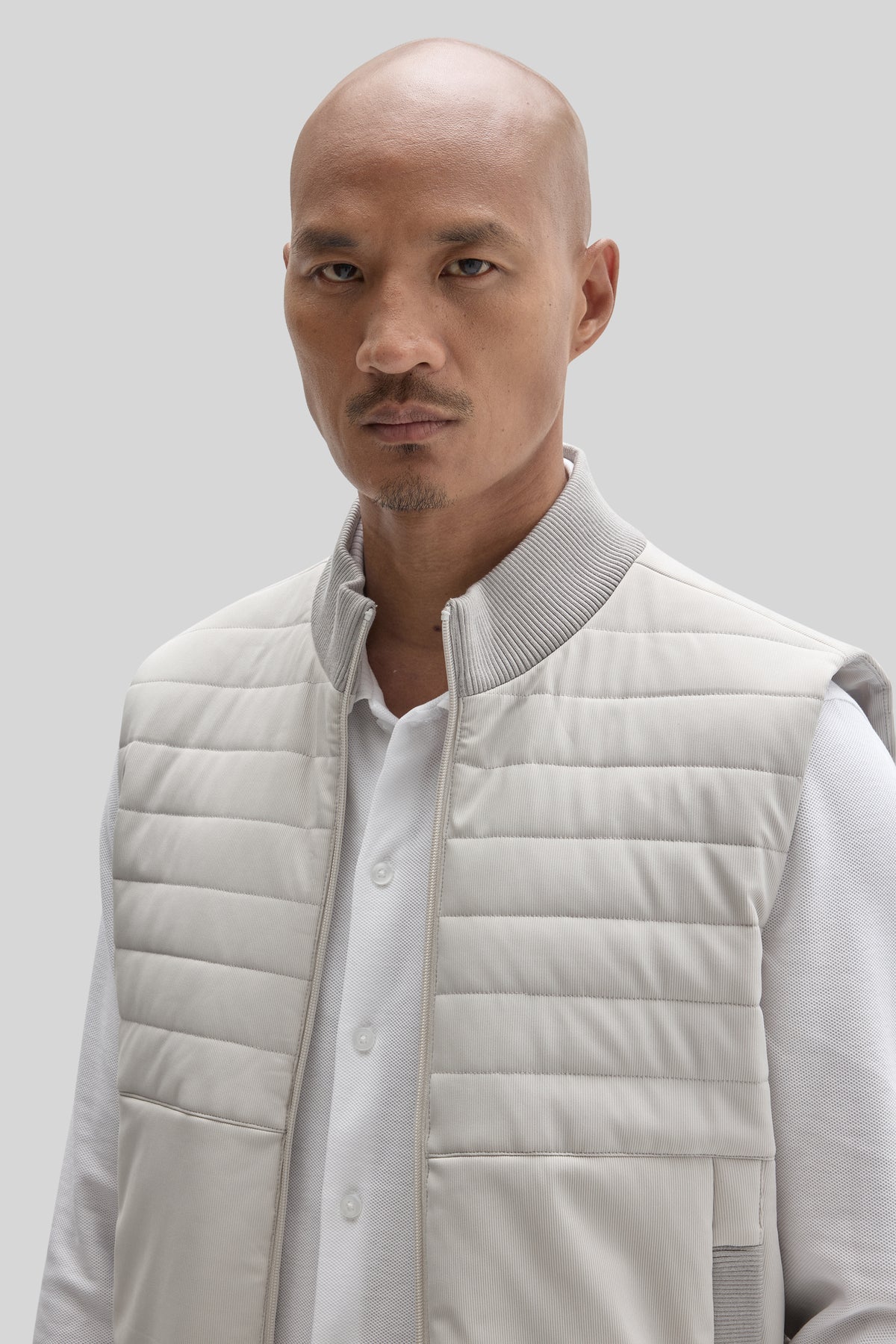 Man wearing cream quilted vest with ribbed collar over white button-up shirt.