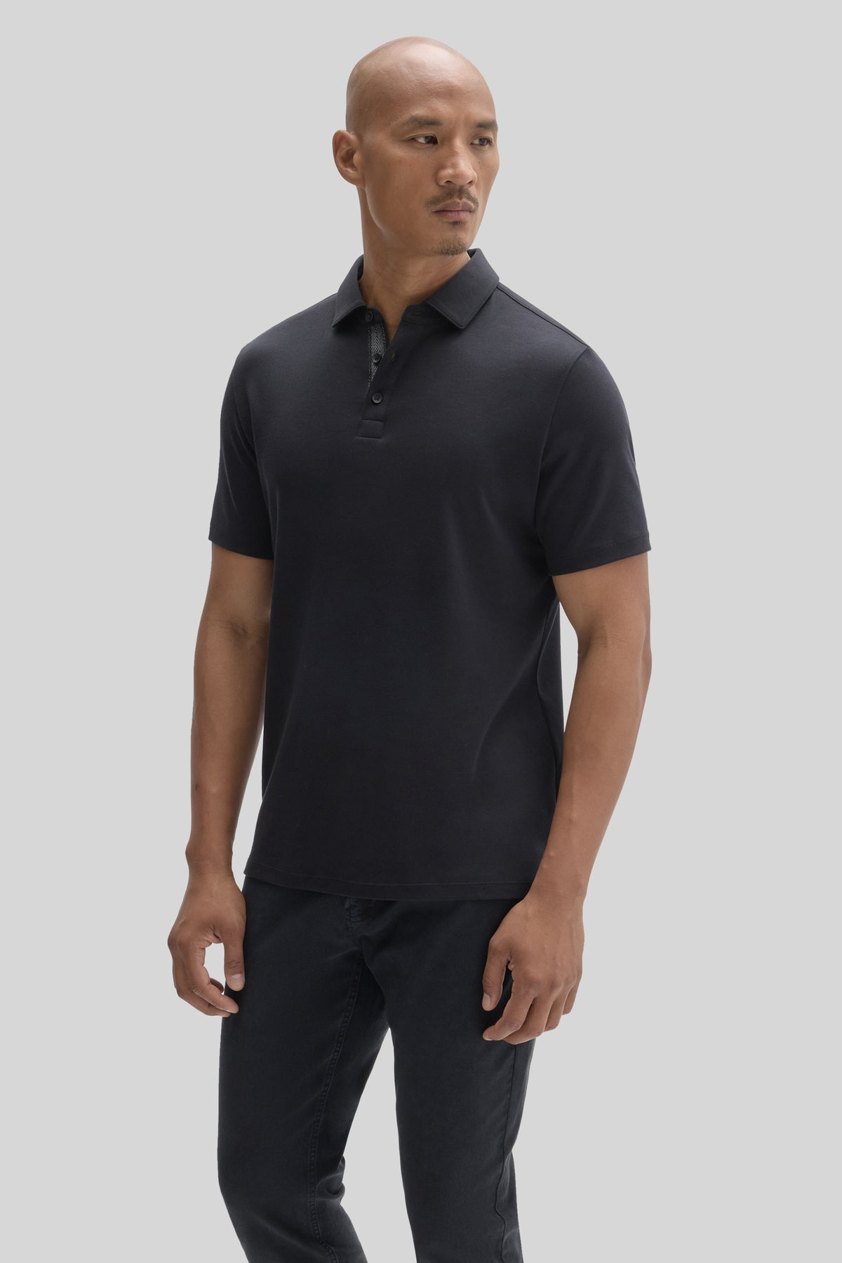 Man wearing black short-sleeve polo shirt with collar and button placket, paired with dark jeans.