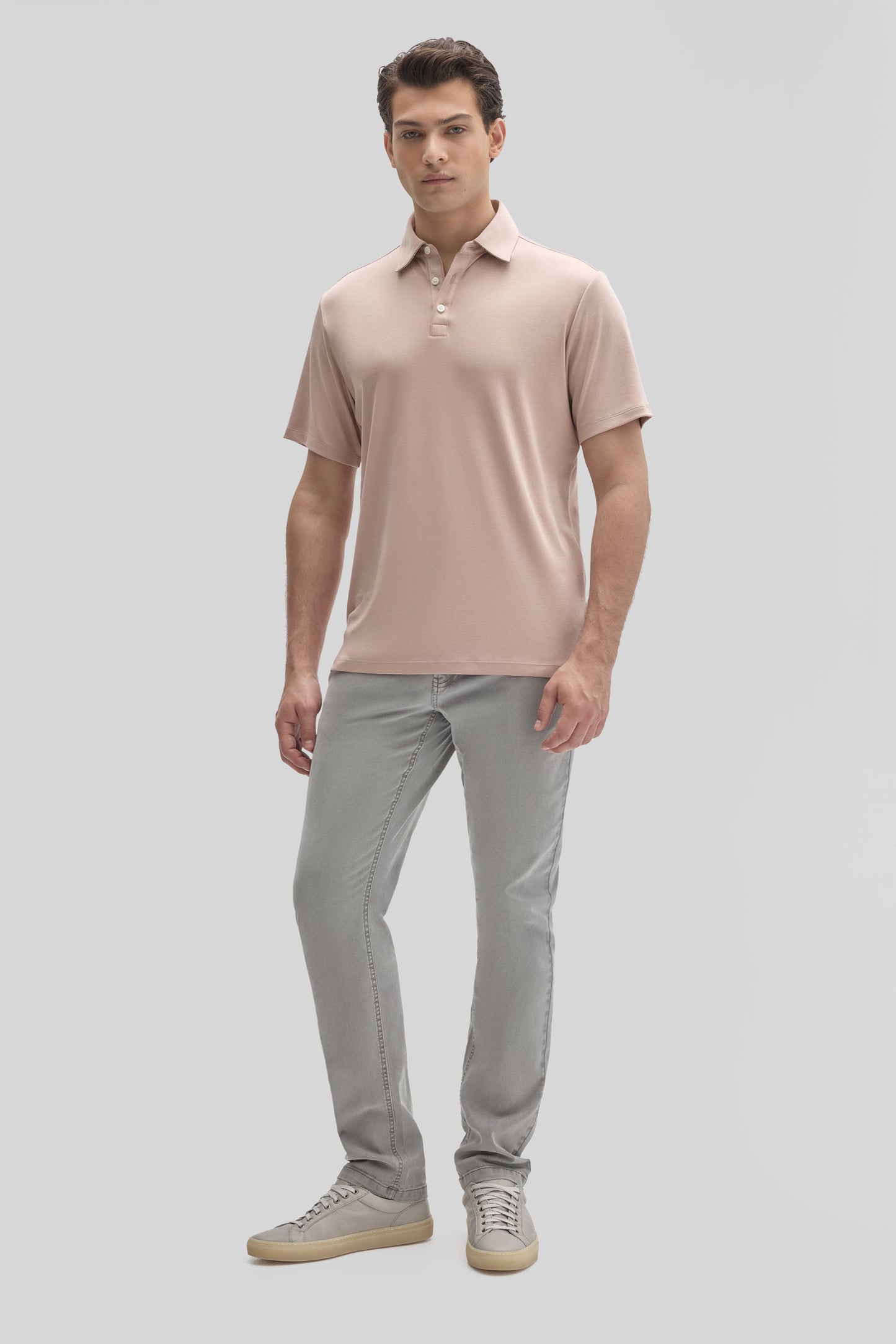 Man wearing blush pink short-sleeve polo shirt with collar and button placket, paired with gray jeans.