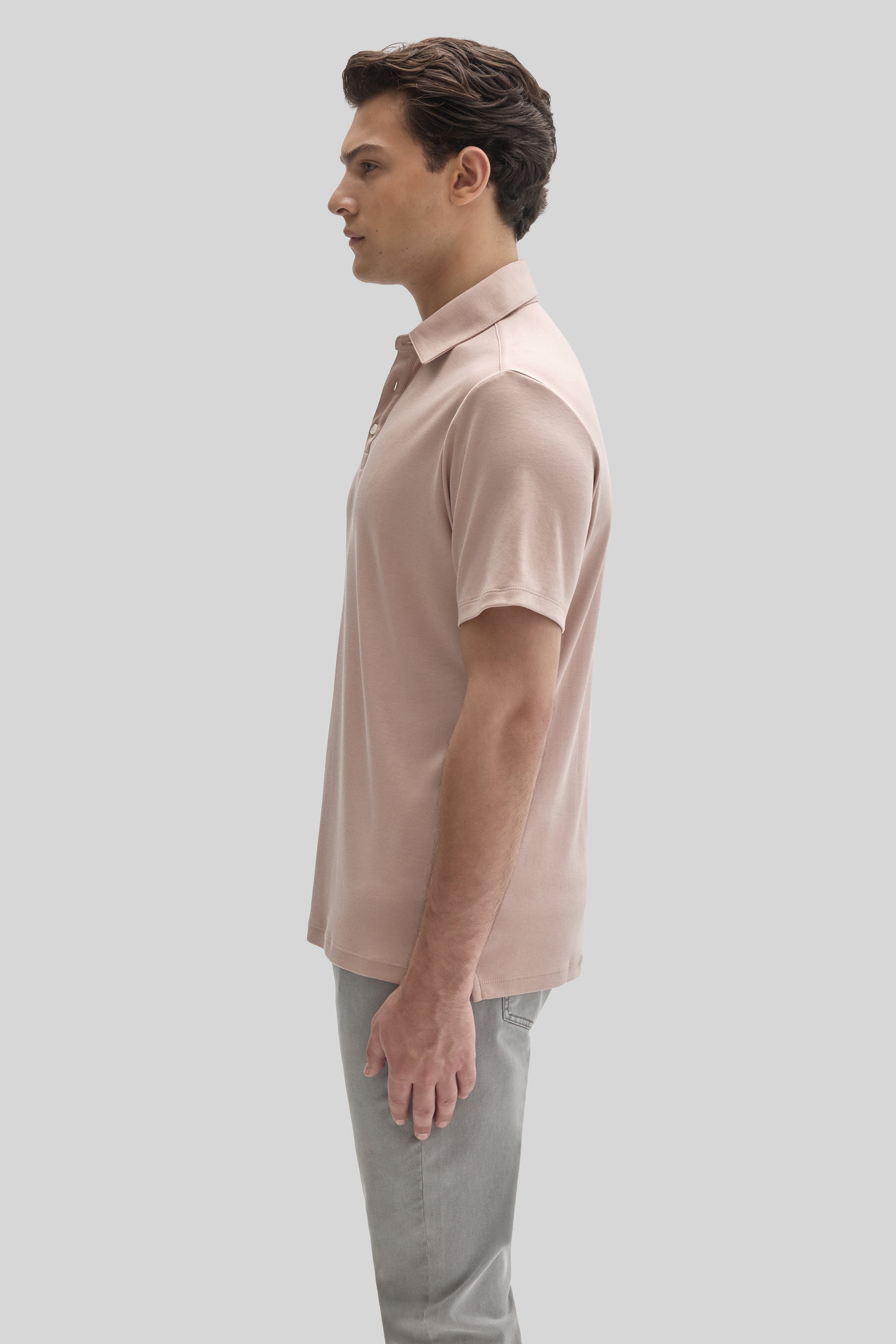 Man wearing a light pink short-sleeve polo shirt with herringbone texture and gray pants, shown in profile view.
