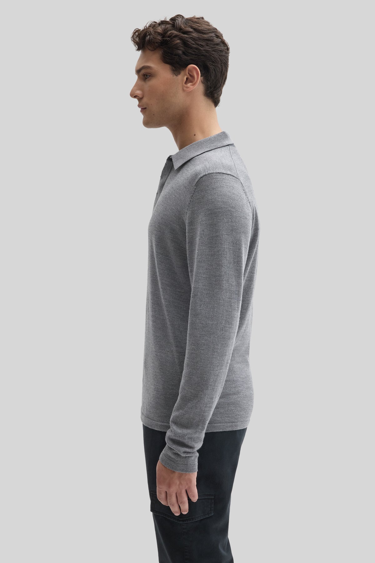 Man wearing a gray long sleeve sweater polo with collar and black pants, shown in side profile.