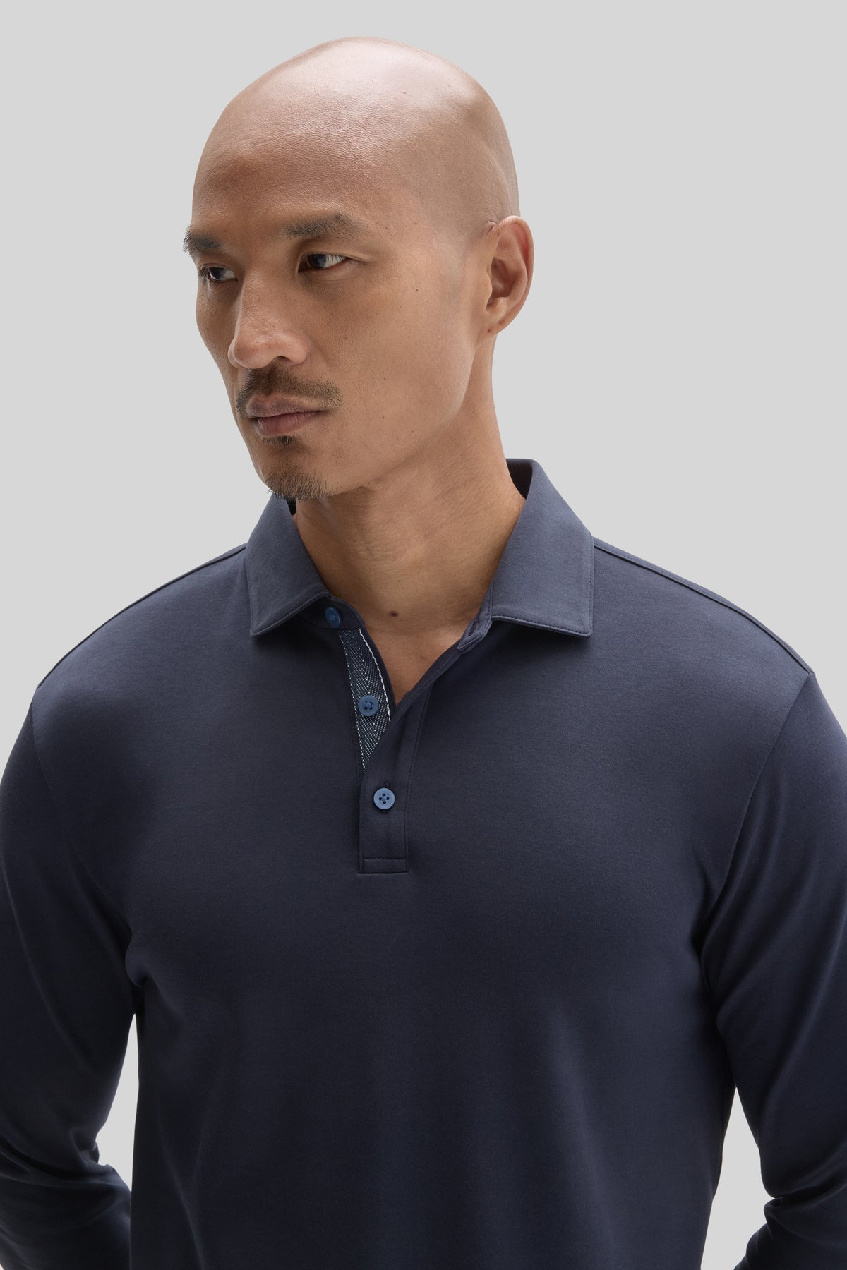 Man wearing dark navy long-sleeve polo shirt with herringbone pattern collar detail and button front closure.