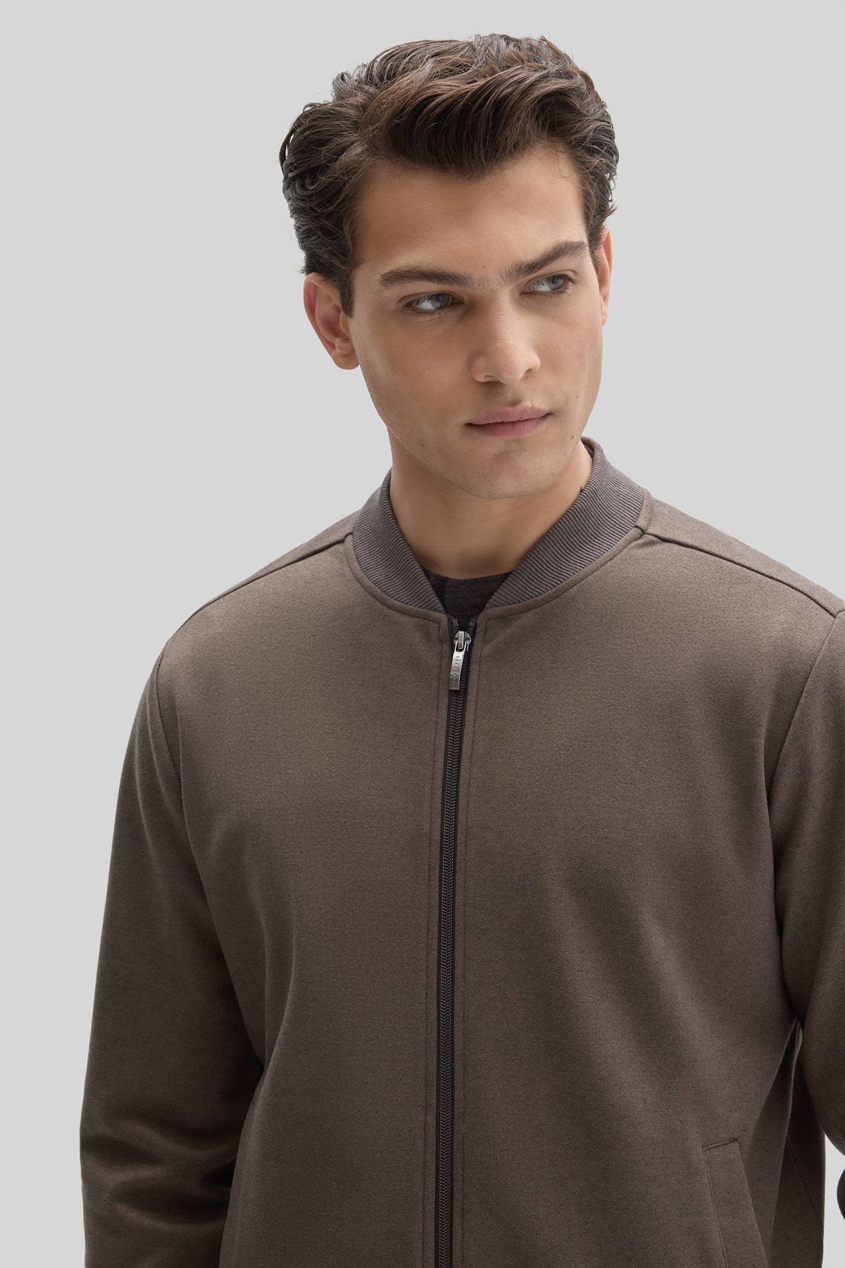 Man wearing taupe baseball collar jacket with full-length zipper and ribbed collar over black shirt.
