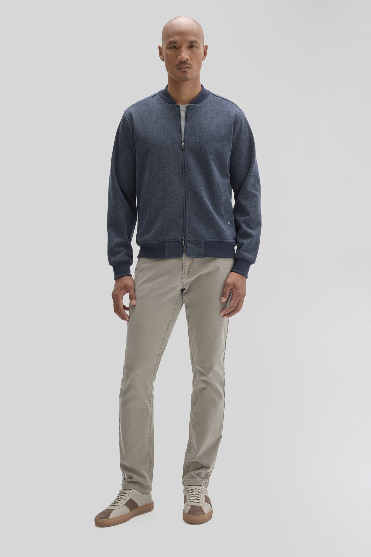 Navy blue baseball collar jacket with full-length zipper worn with beige pants and sneakers.