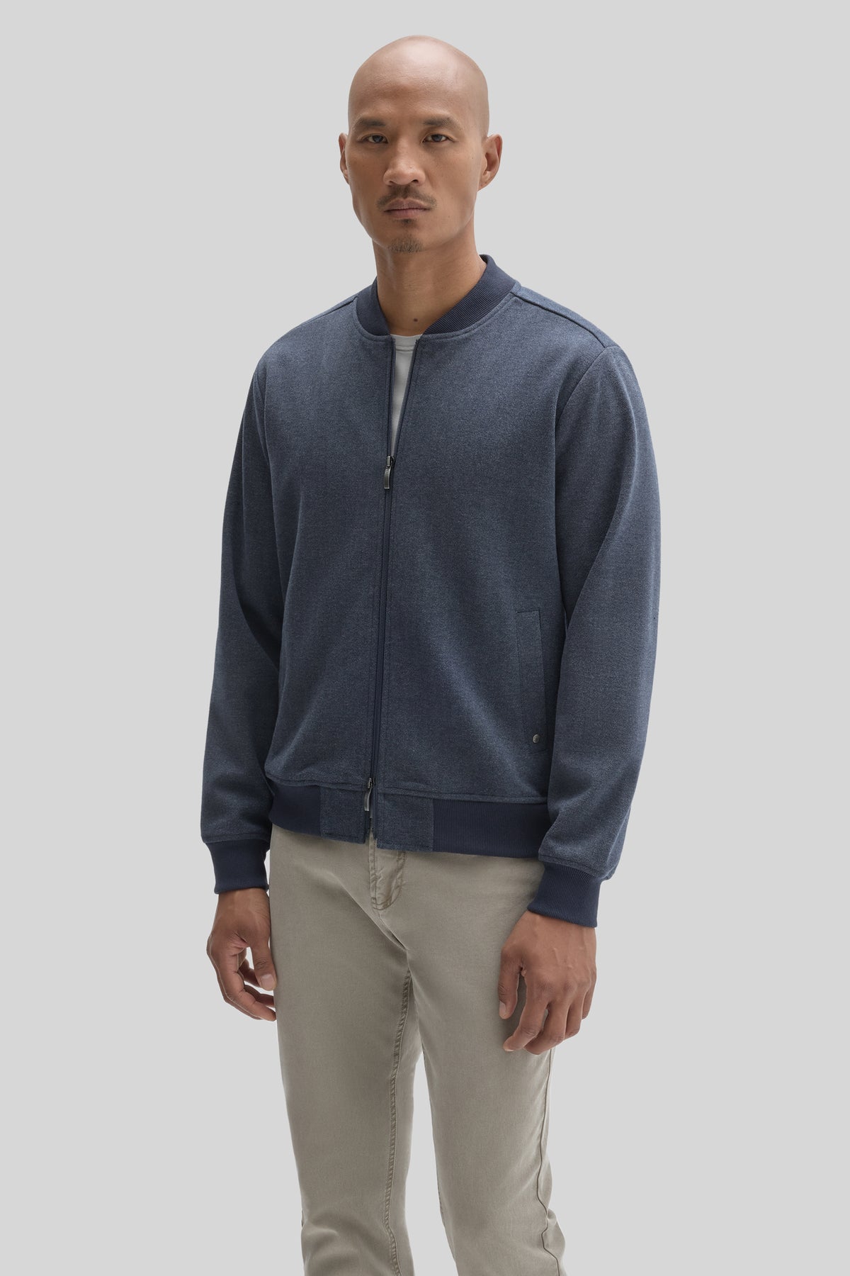 Man wearing dark blue baseball collar jacket with full zip closure and ribbed cuffs over light beige pants.