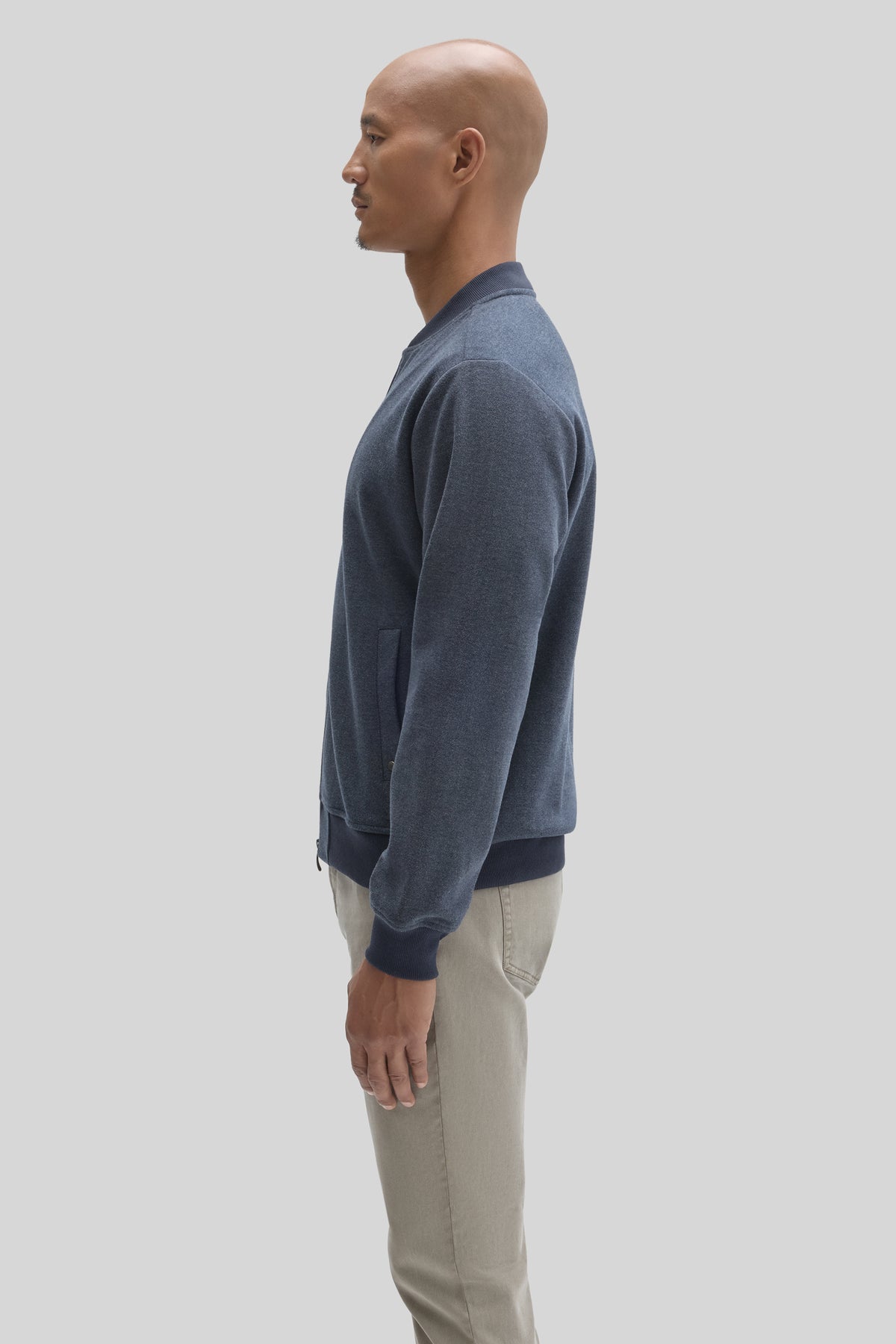 Man wearing blue baseball collar jacket with ribbed cuffs and hem, paired with beige pants.