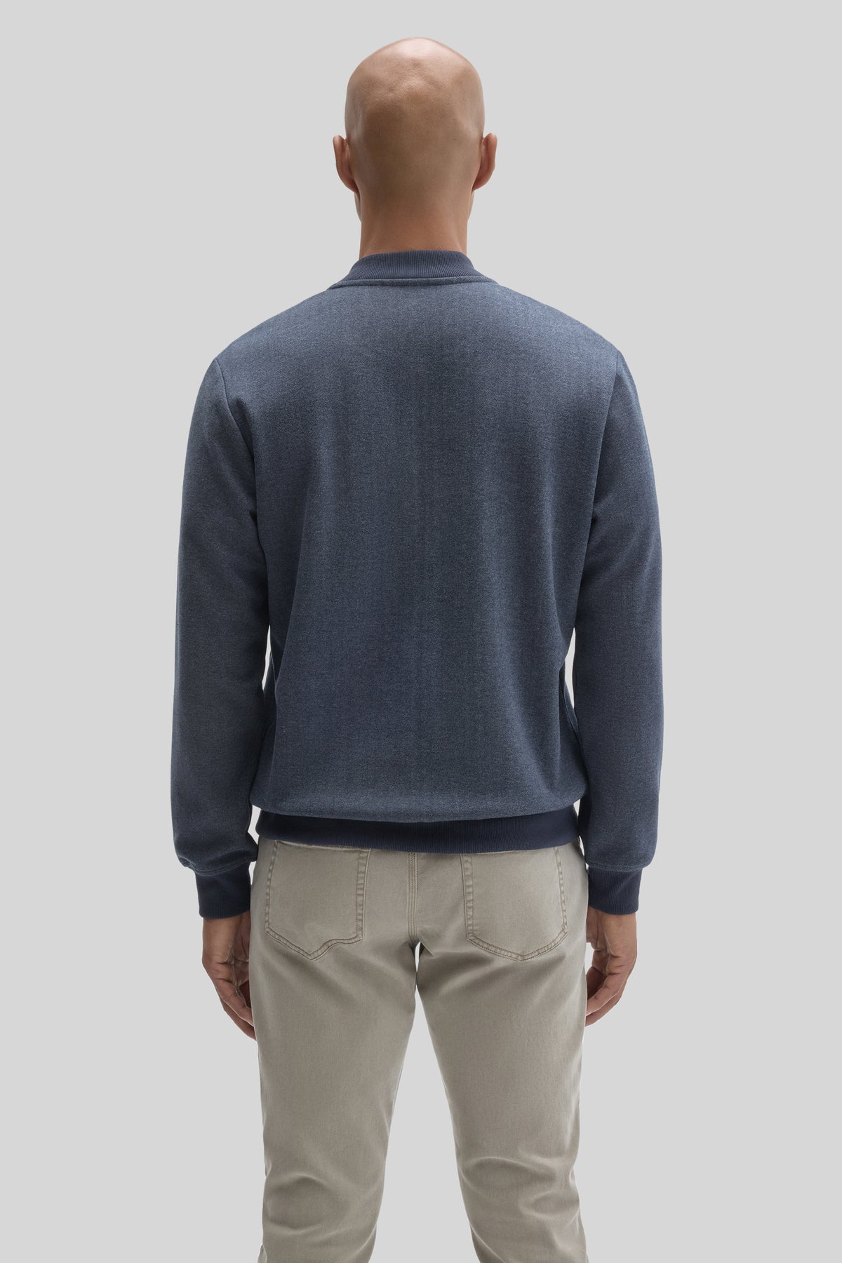 Man wearing blue baseball collar jacket with ribbed trim, shown from back, paired with beige pants.