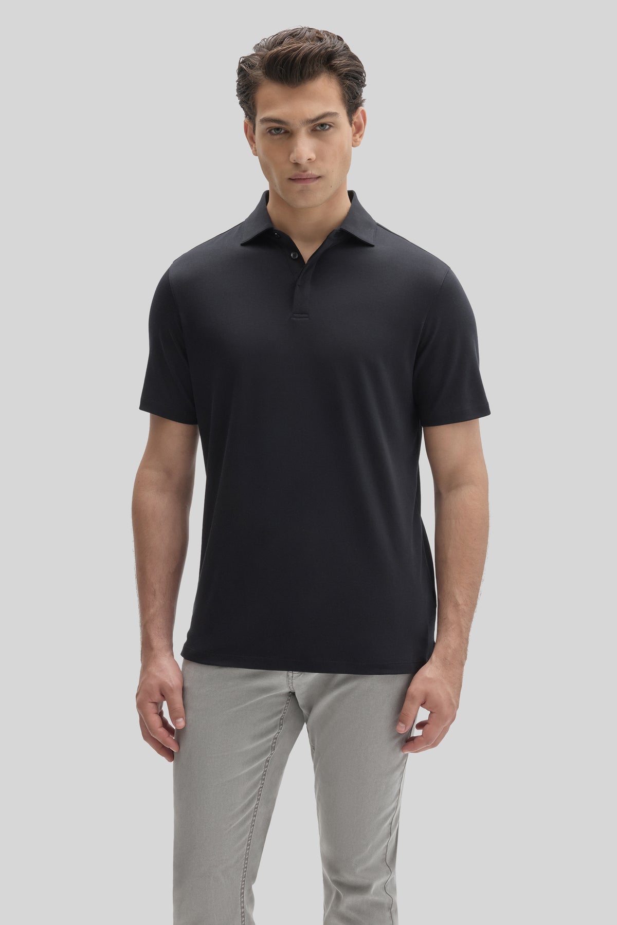 Man wearing black short-sleeve polo shirt with covered placket and gray pants.