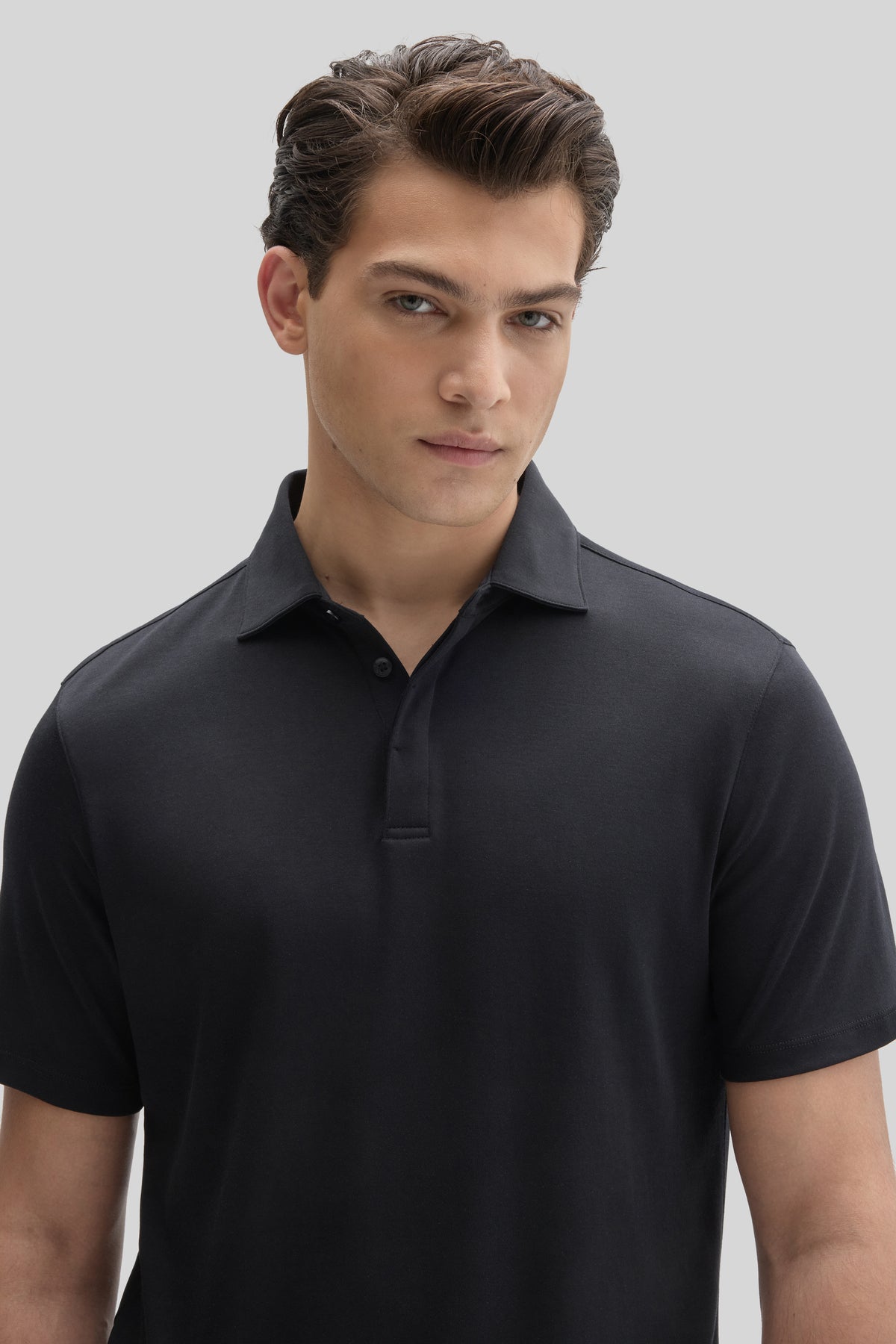 Man wearing black short-sleeve polo shirt with covered placket and collar, shown from chest up.