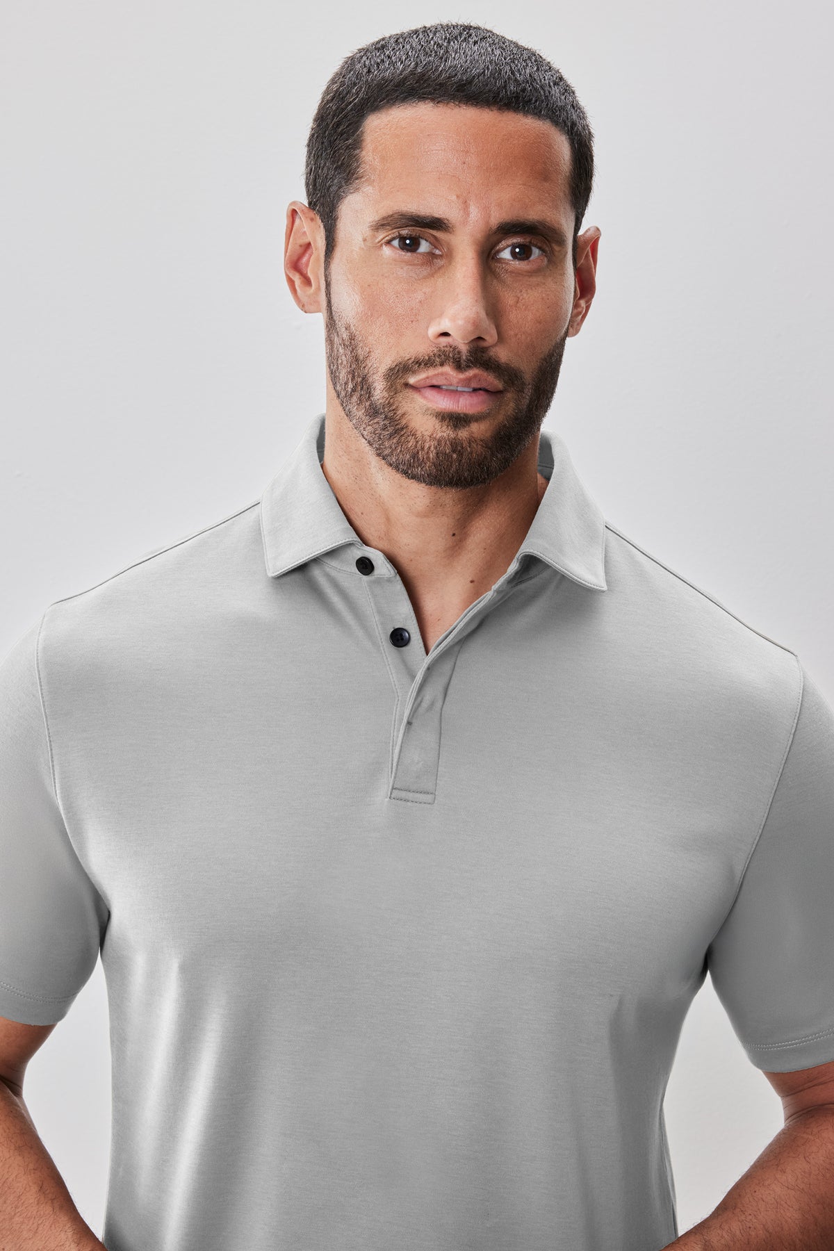 Man wearing light gray polo shirt with white collar and black button placket.