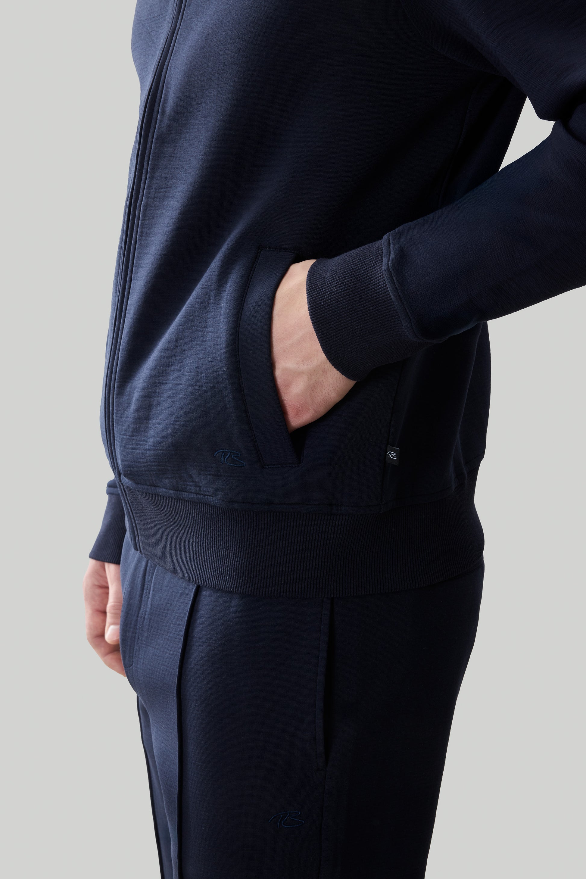 Navy long sleeve full zip jacket with ribbed cuffs, waistband, and front pocket detail.